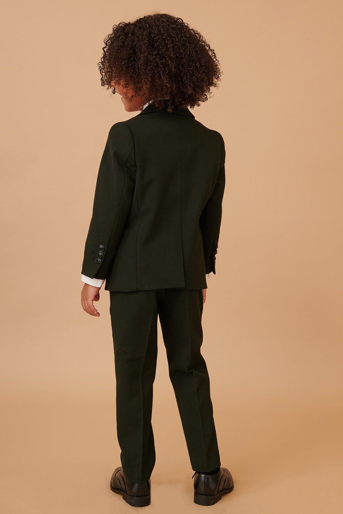 A child with curly hair faces away from the camera, wearing the Marc Darcy BROMLEY Children's Olive Green Check Print Three Piece Suit and black dress shoes.