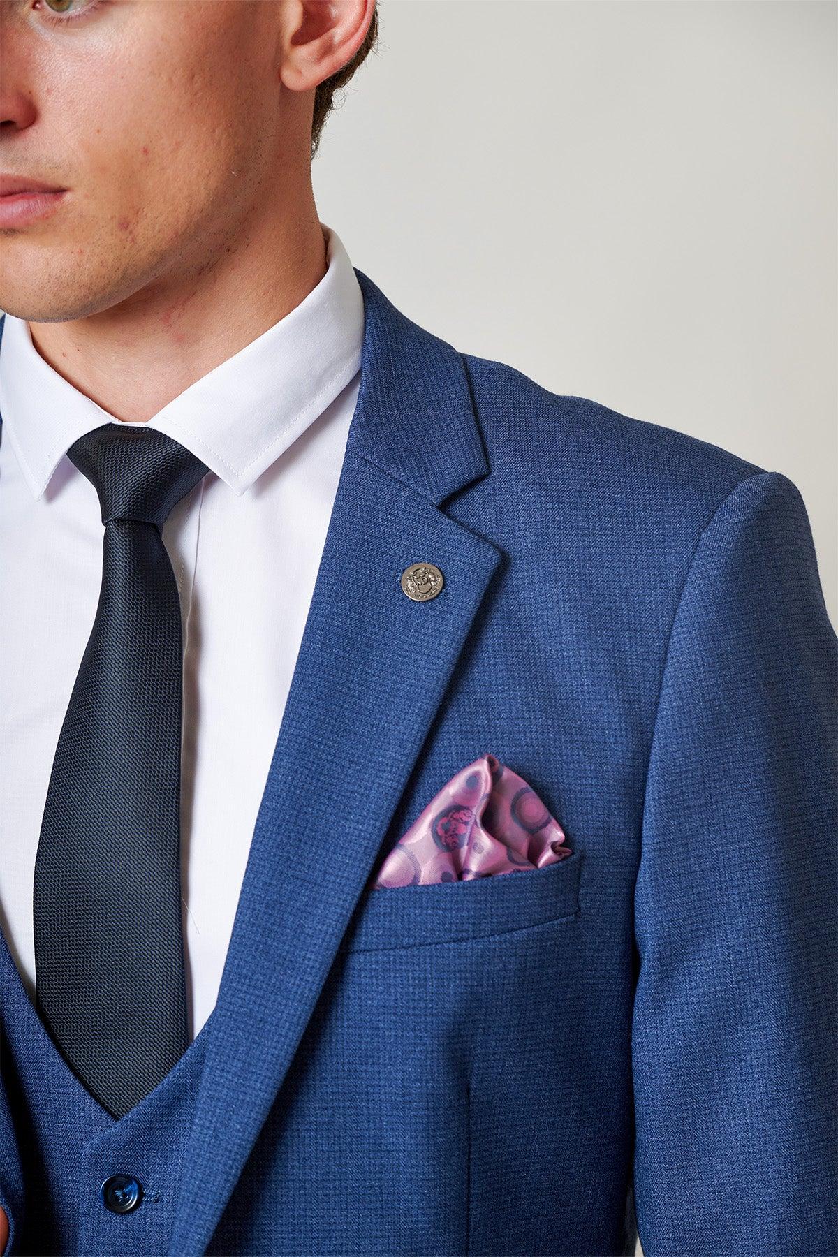 Close up of a man in the Marc Darcy ASHLEY Navy Blue Two Piece Suit, paired with a white shirt, dark tie, and pink patterned pocket square. A silver lapel pin completes this stylish menswear look.