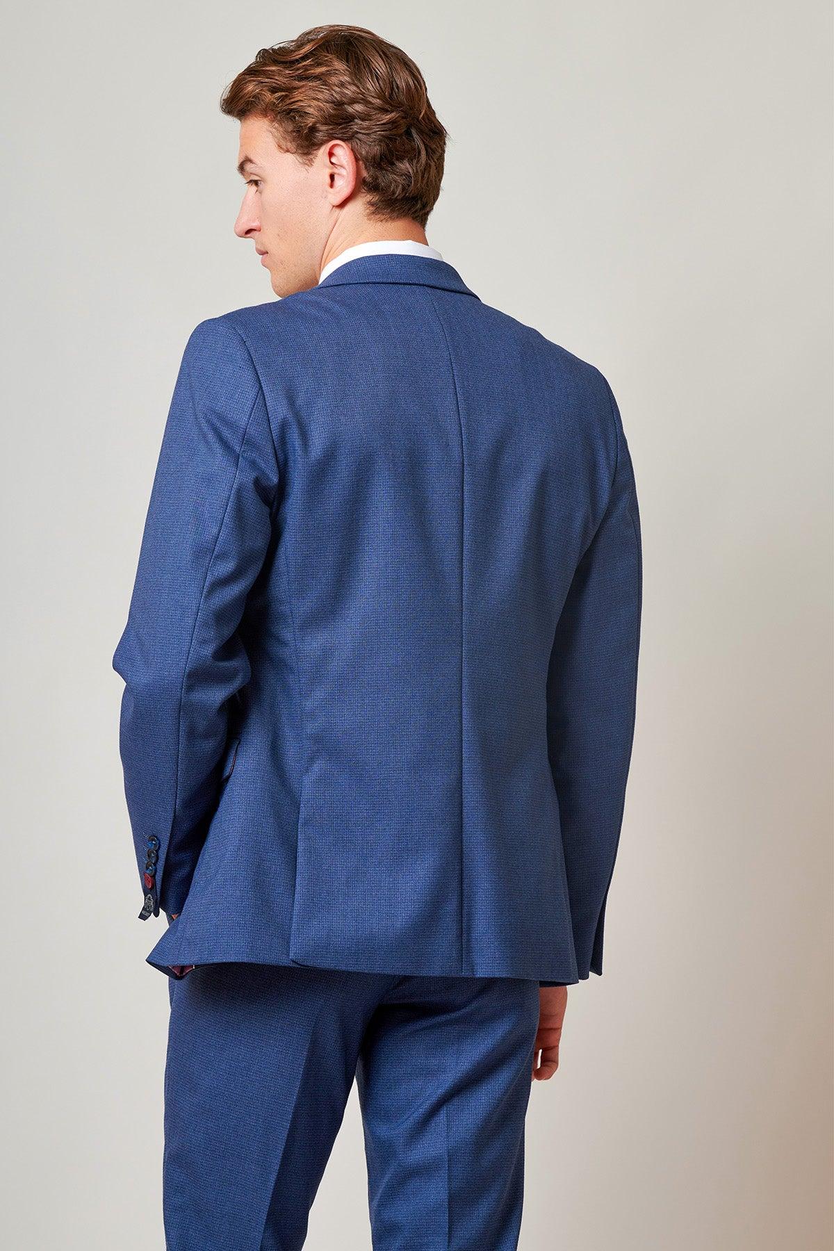 A man stands with his back to the camera, glancing over his left shoulder, dressed in the Marc Darcy ASHLEY Navy Blue Two Piece Suit with matching pants and a white shirt, set against a plain light background.