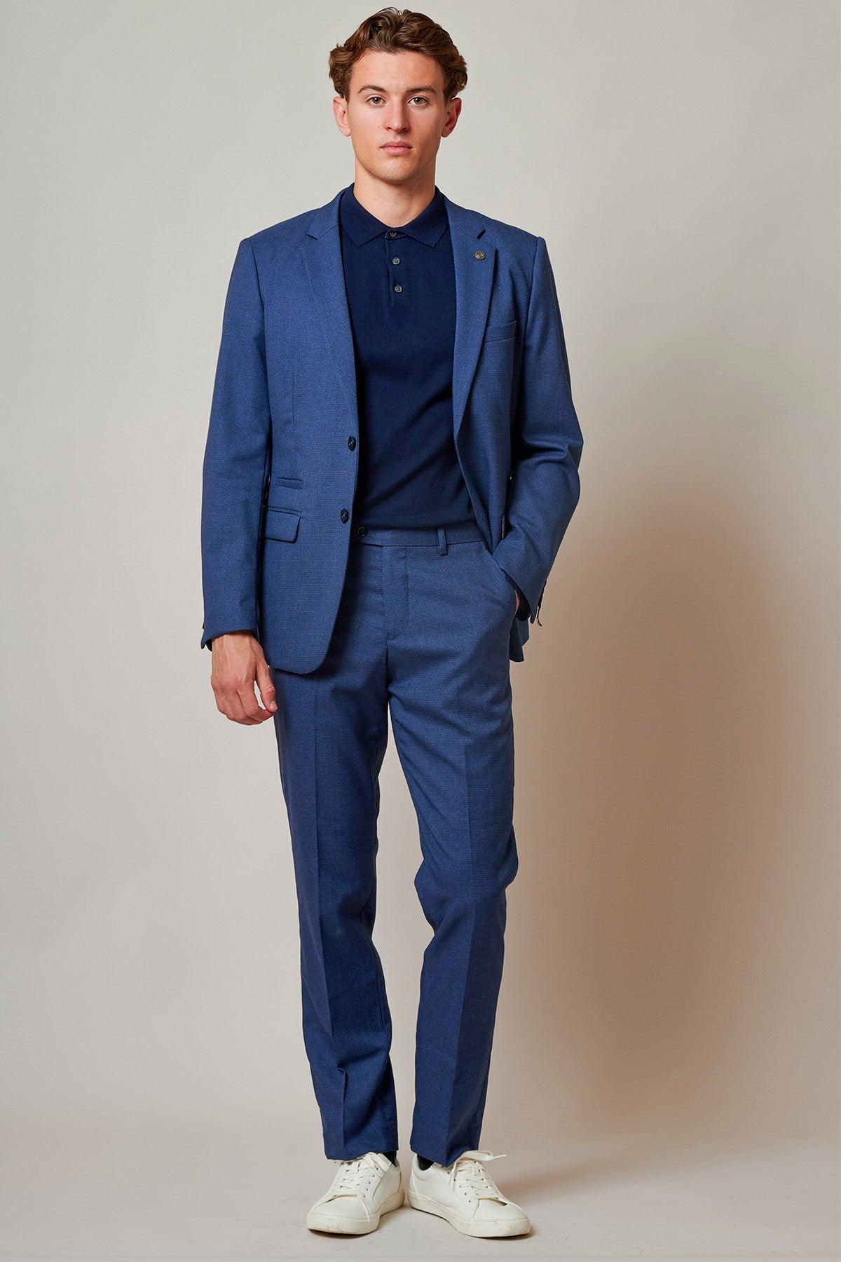 A young man wears the ASHLEY - Navy Blue Two Piece Suit by Marc Darcy, styled with a navy polo shirt and white sneakers.