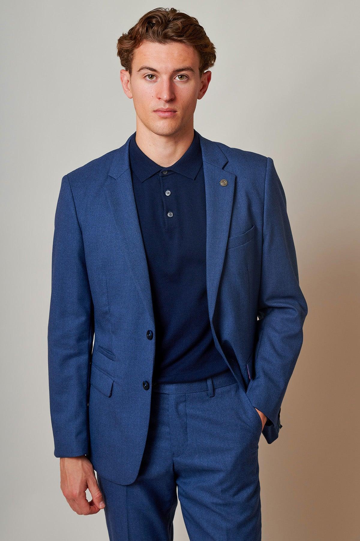 A man wears the Marc Darcy ASHLEY Navy Blue Two Piece Suit with a navy polo shirt, standing with his hand in his pocket.