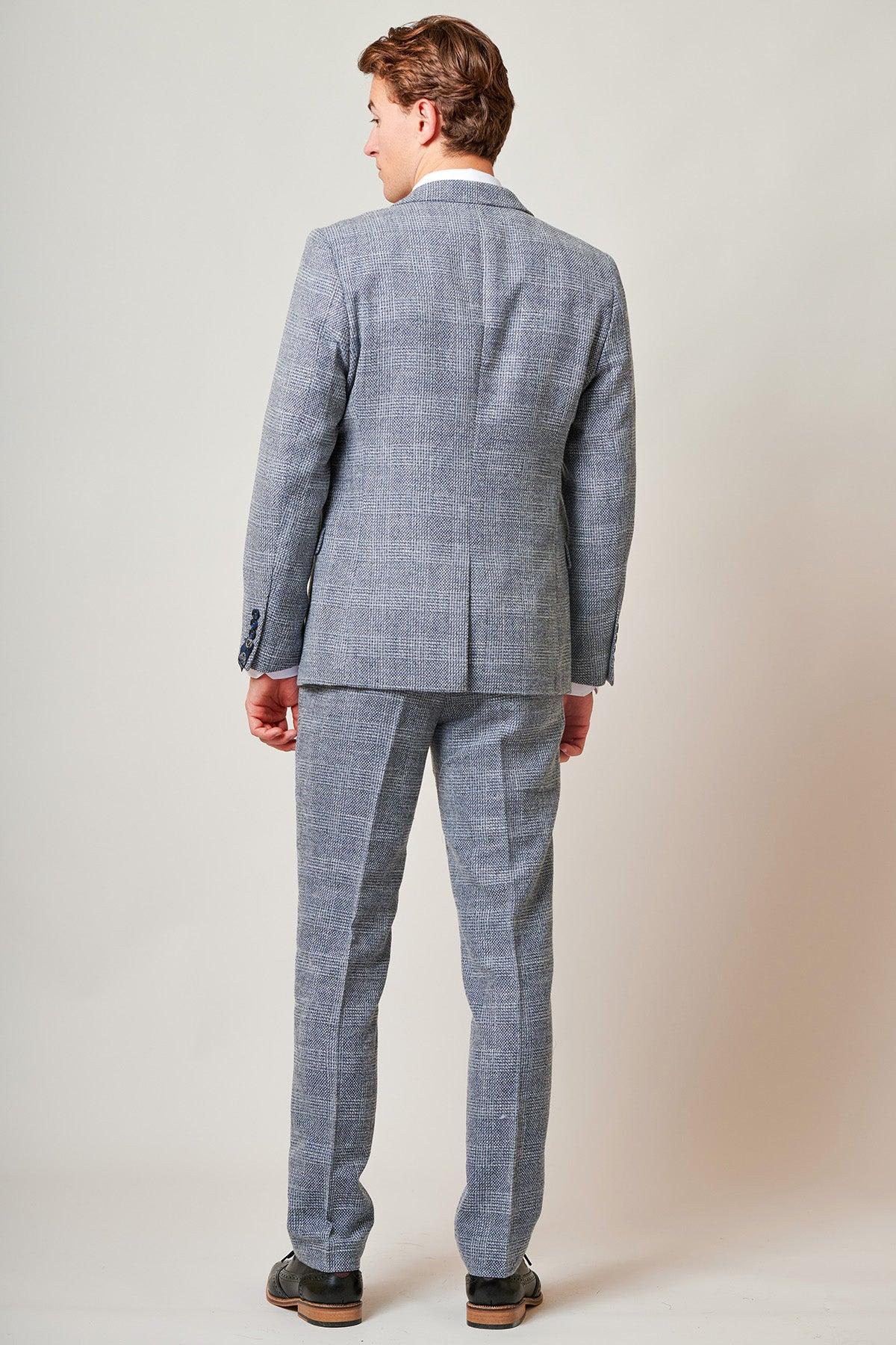 A man faces away from the camera, wearing the marcdarcy Everton Collection Tim Iroegbunam in KRIS Sky Blue Tweed Suit with matching trousers and dark shoes against a plain light background.
