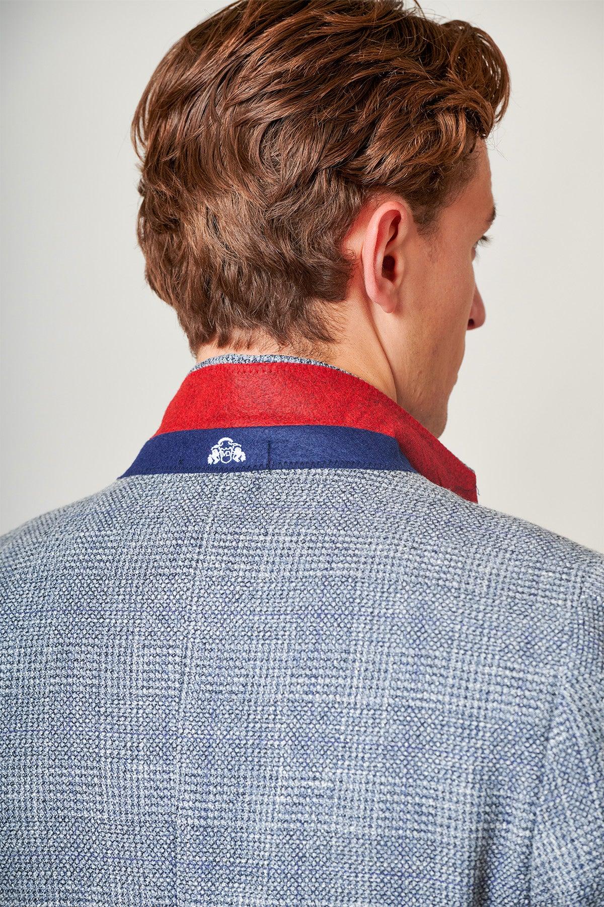 Close-up of the back of a man's head and shoulders wearing marcdarcy’s The Everton Collection | Tim Iroegbunam in KRIS Sky Blue Tweed Suit, featuring a blue Prince of Wales check and distinctive red and blue collar. He has brown hair.