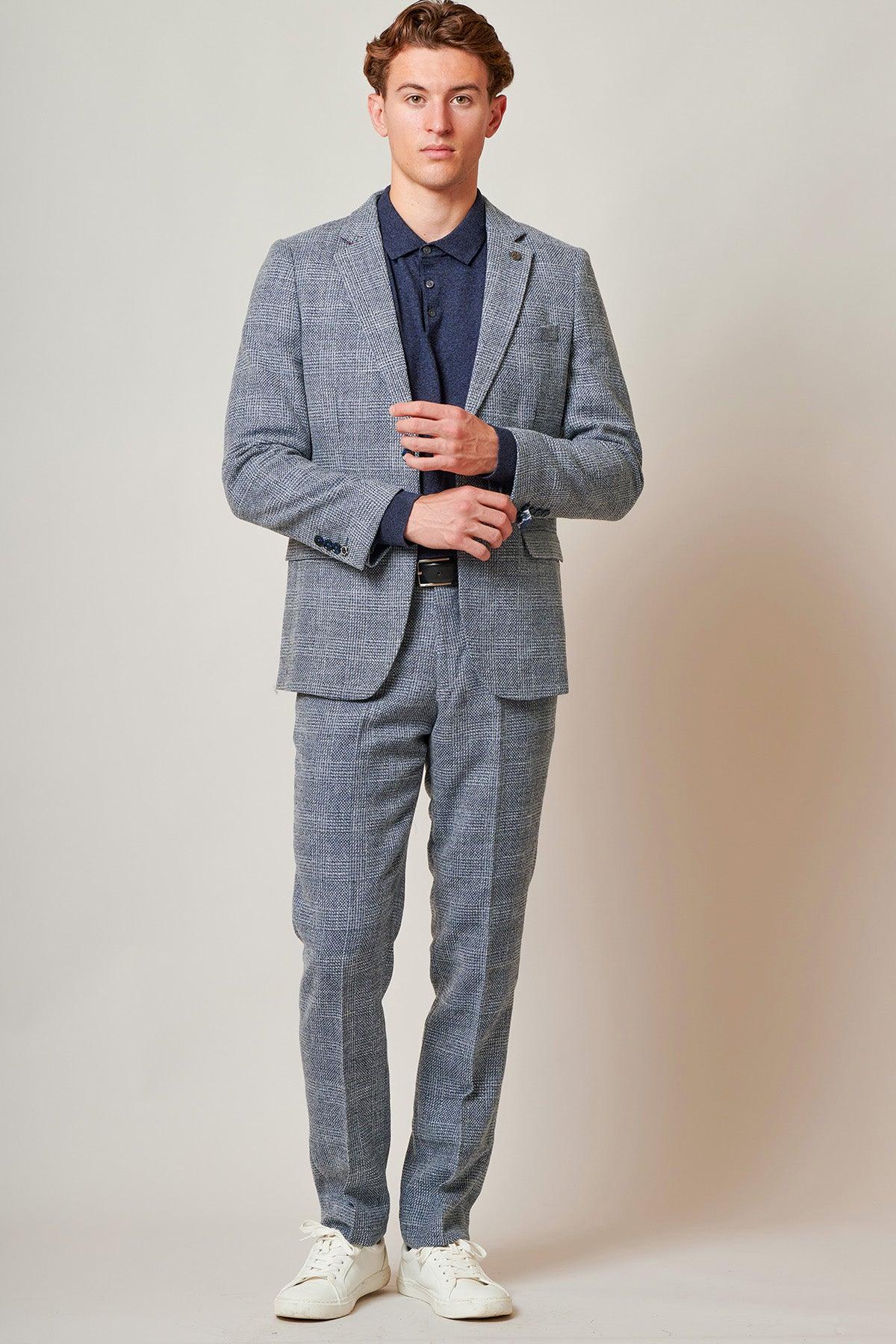 Tim Iroegbunam models The Everton Collection KRIS Sky Blue Tweed Suit by marcdarcy, styled with a dark blue polo shirt and white sneakers, posing against a plain background.