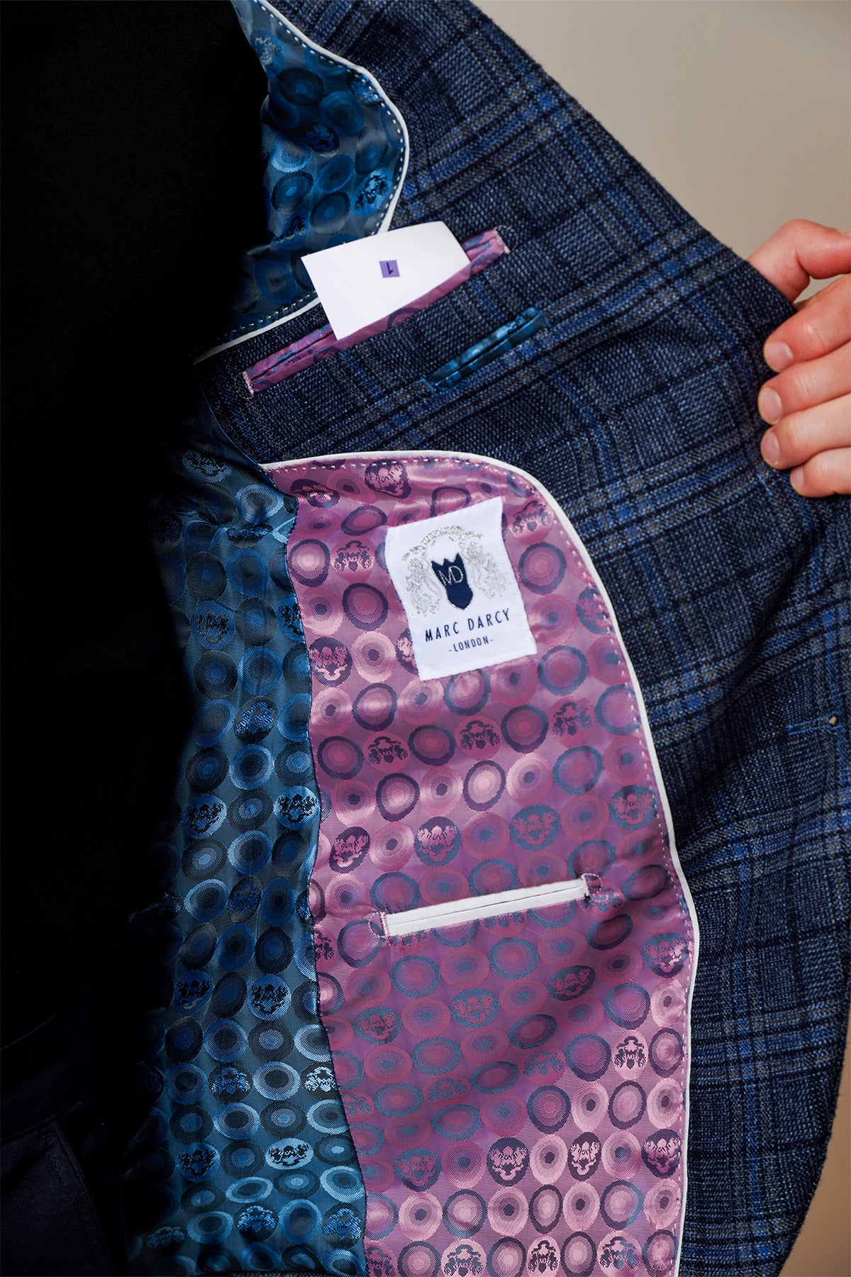 Someone holds open the ANDY - Blue Check Blazer by Marc Darcy, revealing a vibrant blue and pink patterned lining, a white Marc Darcy label, and a business card in the pocket—classic heritage style with modern flair.