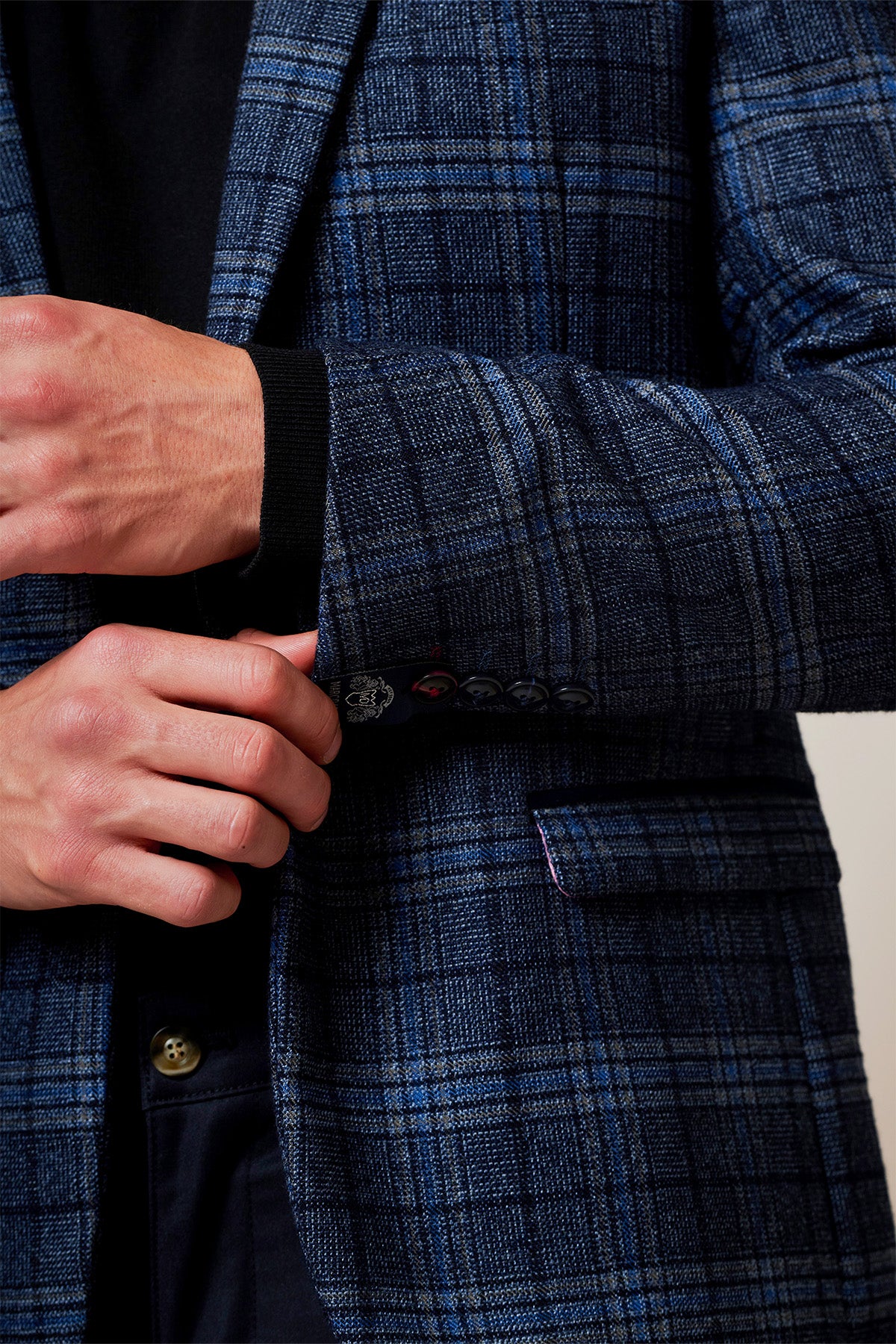 Close-up of a man's hands adjusting the cuff of the ANDY Blue Check Two Piece Suit by Marc Darcy, with slim fit tailoring, dark buttons, and a black ribbed cuff underneath for a modern touch and refined detail.