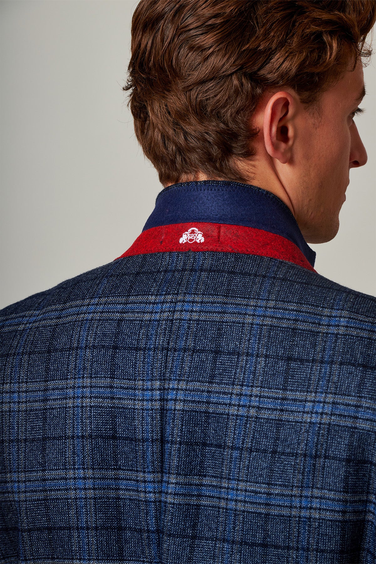 A man with brown hair is seen from behind wearing the Marc Darcy ANDY - Blue Check Blazer, which features a red collar detail and a small white embroidered logo on the back of the collar.