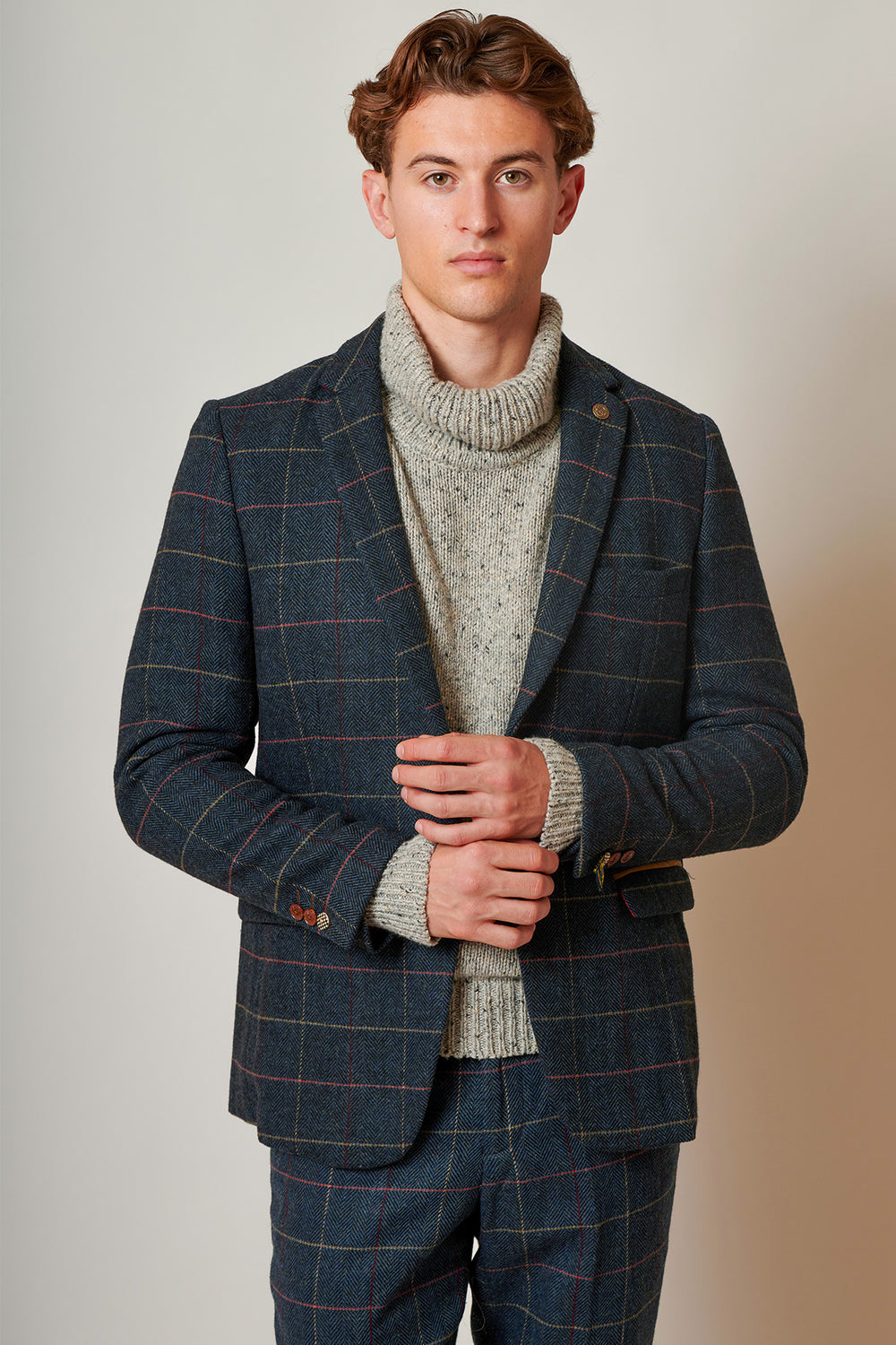 A person wearing an ETON-Navy Blue Tweed Check Blazer by marcdarcy and a chunky gray turtleneck stands against a neutral background. The individual with short brown hair looks directly at the camera with a neutral expression.