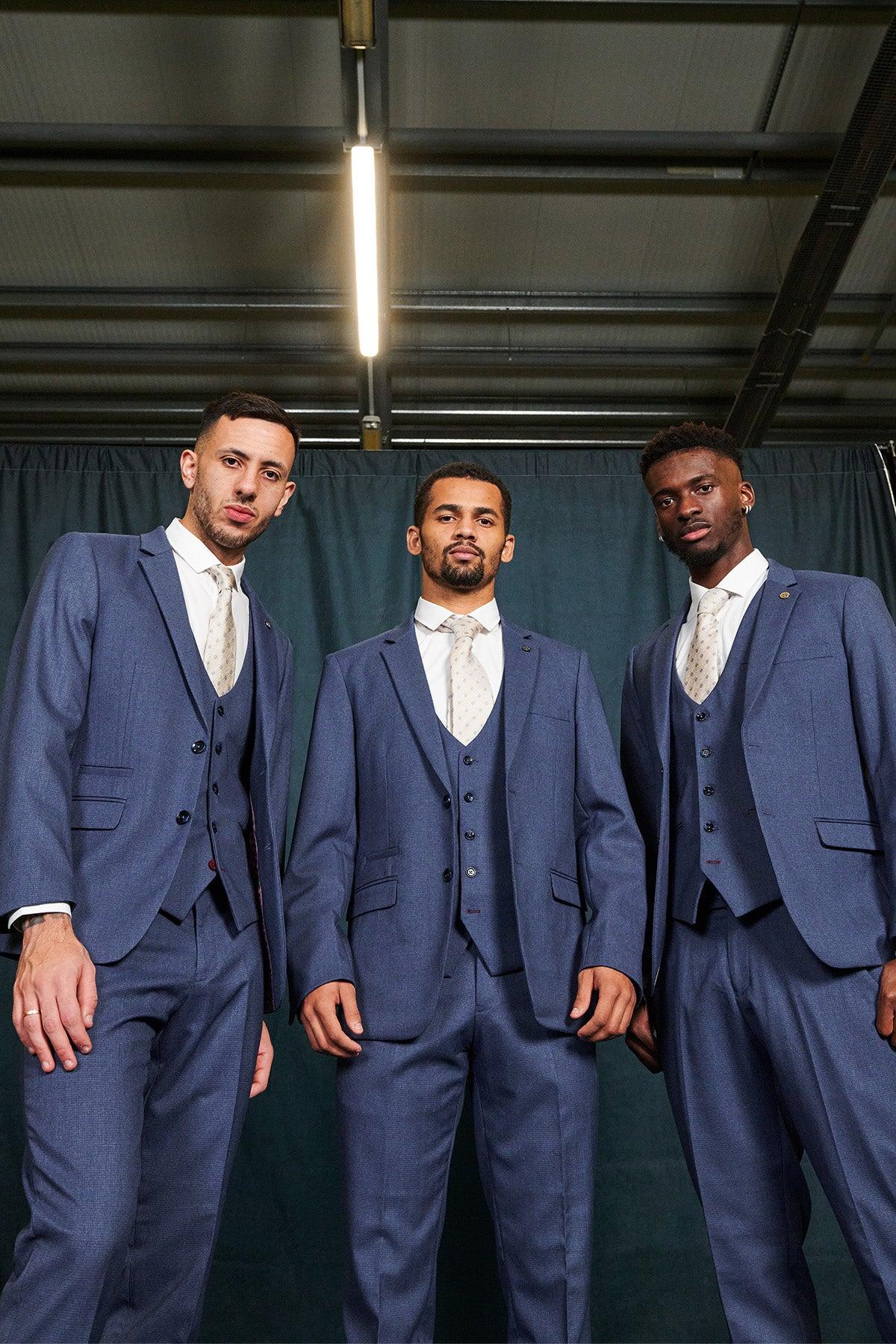 Three men stand in navy blue three piece suits and patterned ties, highlighting the elegance of Marc Darcy’s Everton Collection, featuring the Iliman Ndiaye in ASHLEY Navy Blue Three Piece Suit.
