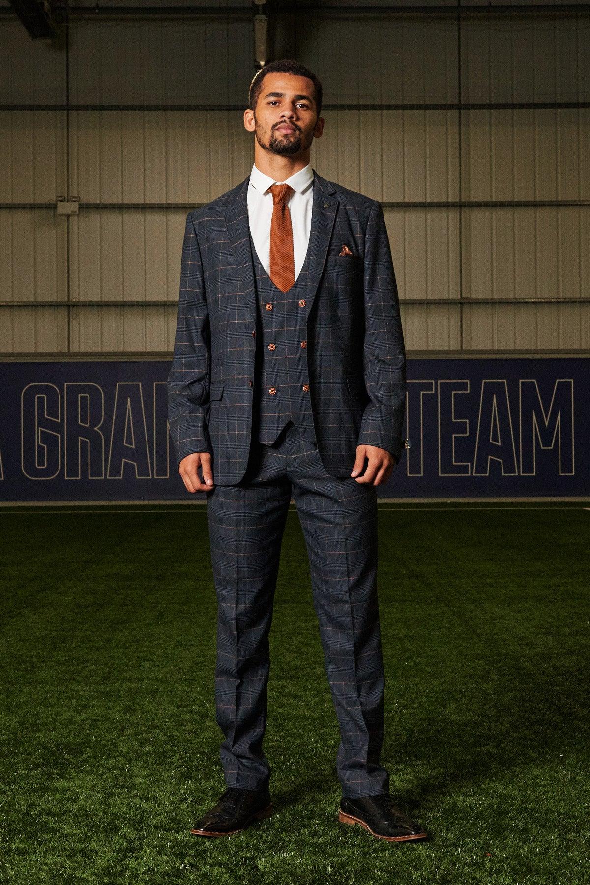 Iliman Ndiaye wears the marcdarcy JENSON Marine Navy Check Suit from The Everton Collection, standing on a turf field in front of a blue banner.