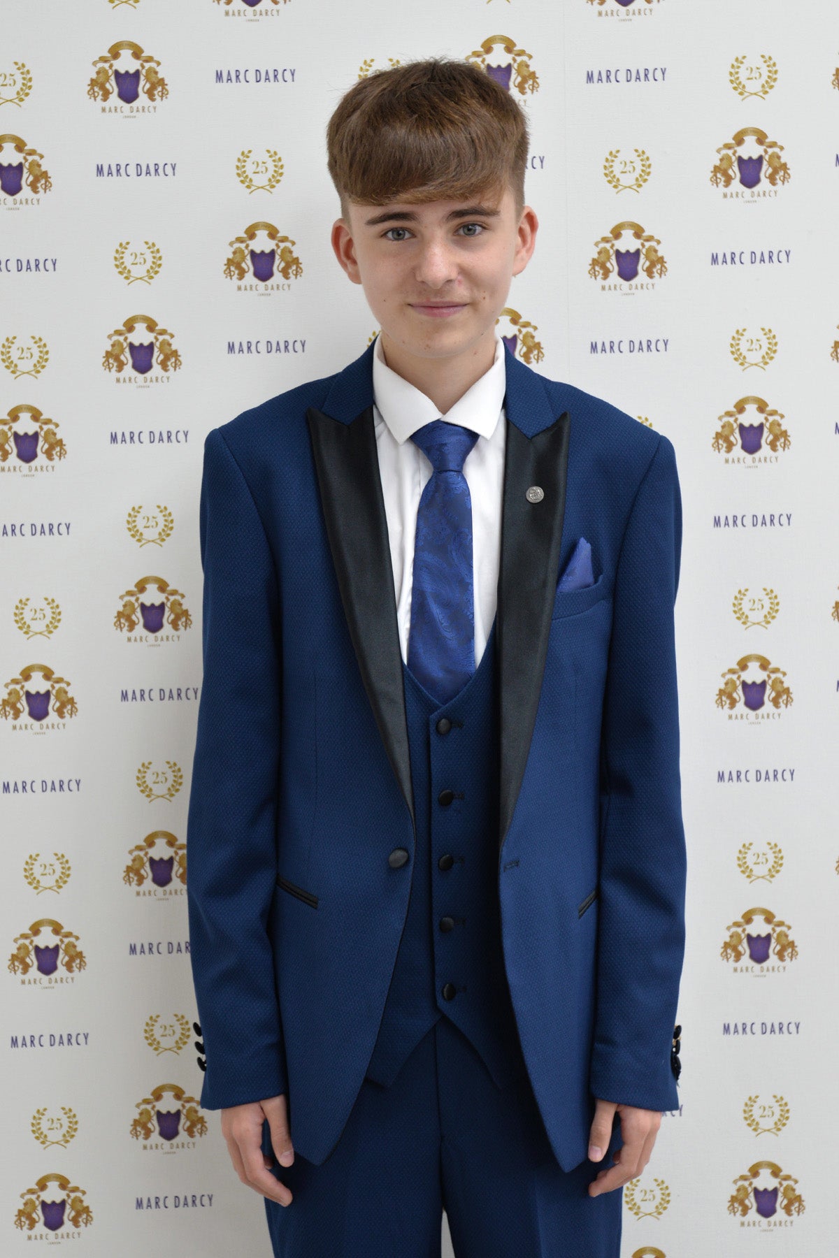 Charlie Wrenshall as Liam Connor wears the marcdarcy DALTON Royal Blue Tux Suit, paired with a blue patterned tie, posing before a white backdrop with the Marc Darcy logo.
