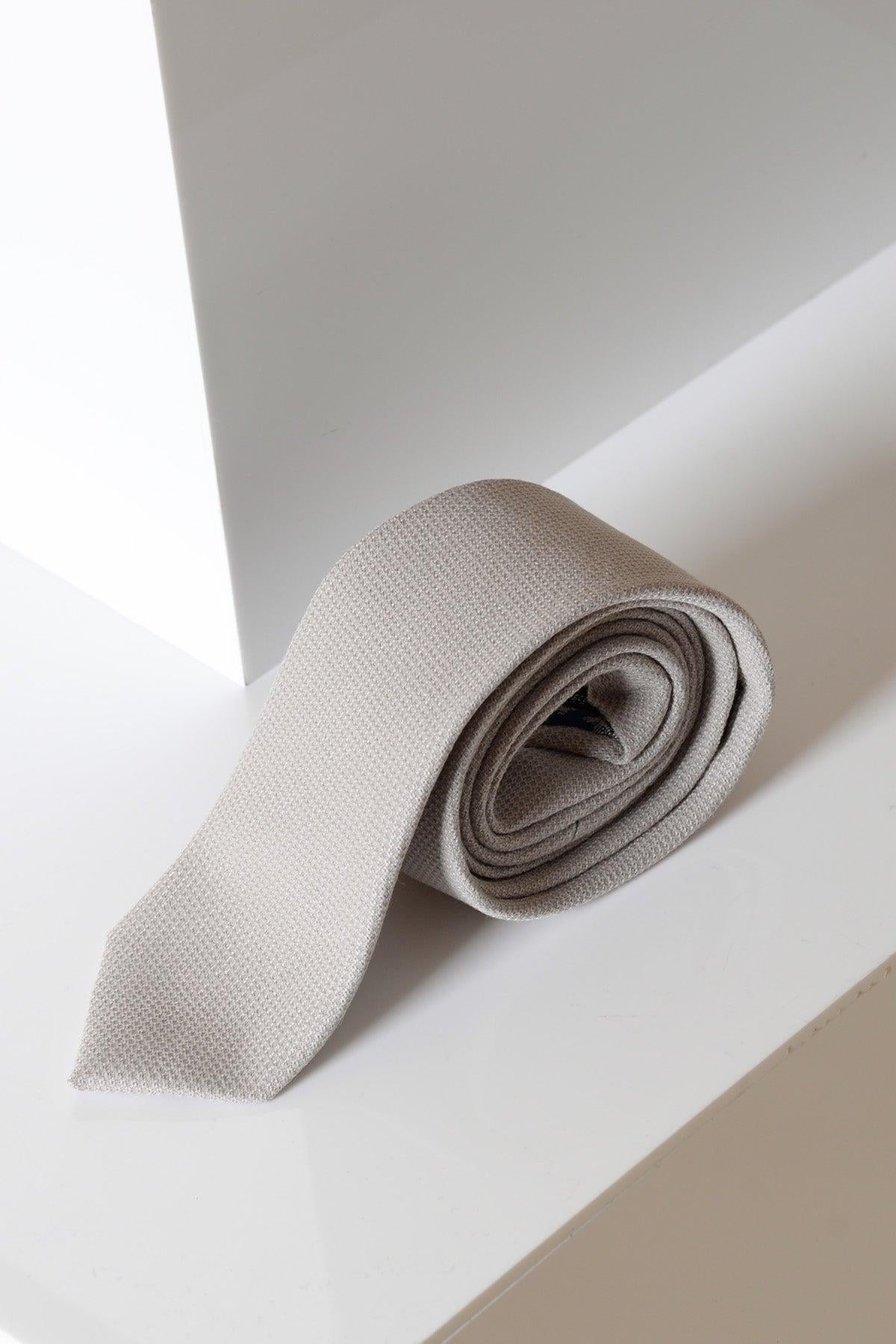 The HM5 - Stone Tie by Accessory, in light gray with a textured finish, is neatly rolled on a glossy white surface near a corner, ideal for formalwear or matching with an HM5 suit under soft lighting.