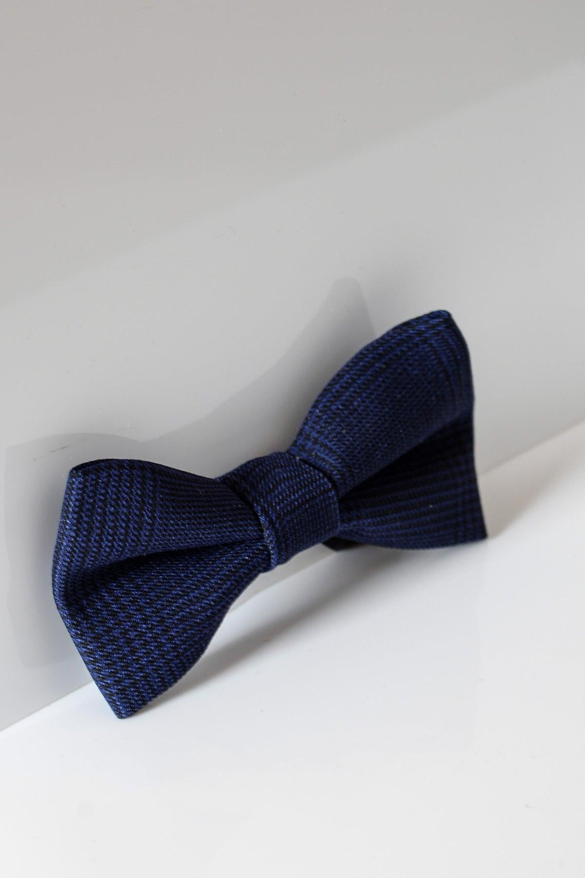 The BROMLEY - Navy Check Bow Tie by Accessory features a subtle checkered pattern—perfect for weddings or formal looks—set against a white and light gray background.