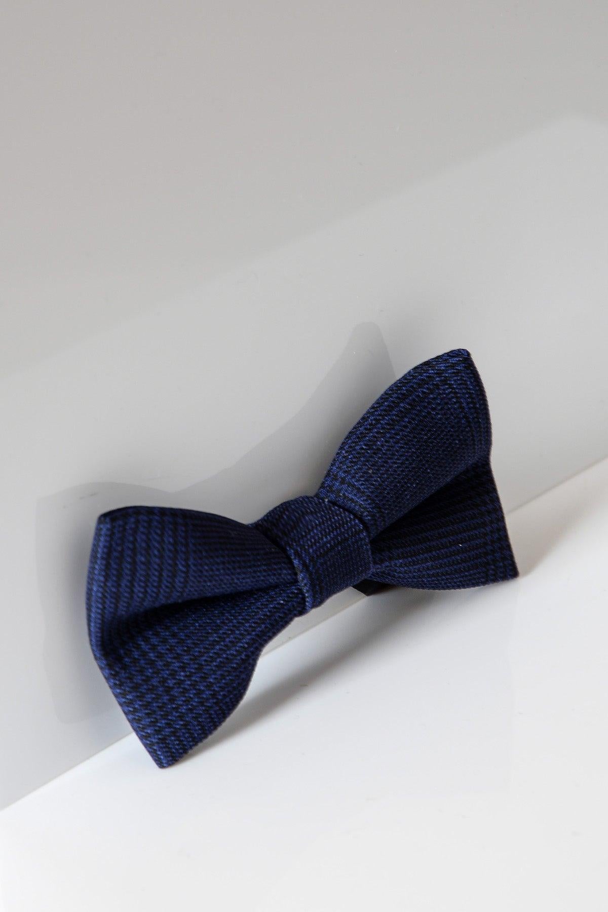 The BROMLEY - Navy Check Bow Tie by Accessory features a stylish check pattern, ideal for formalwear or weddings, and is displayed against a clean white and light gray background.