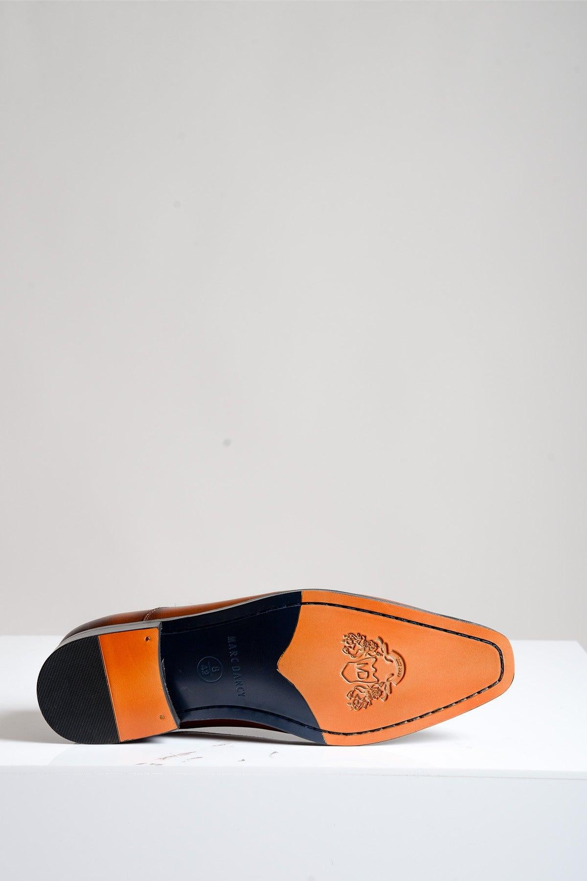 The Marc Darcy JAKE - Tan Leather Contrast Oxford Shoe is displayed sole-up on a white surface, showing its orange-brown full grain leather sole with black edges and a lion crest logo near the toe—ideal for formal occasions.