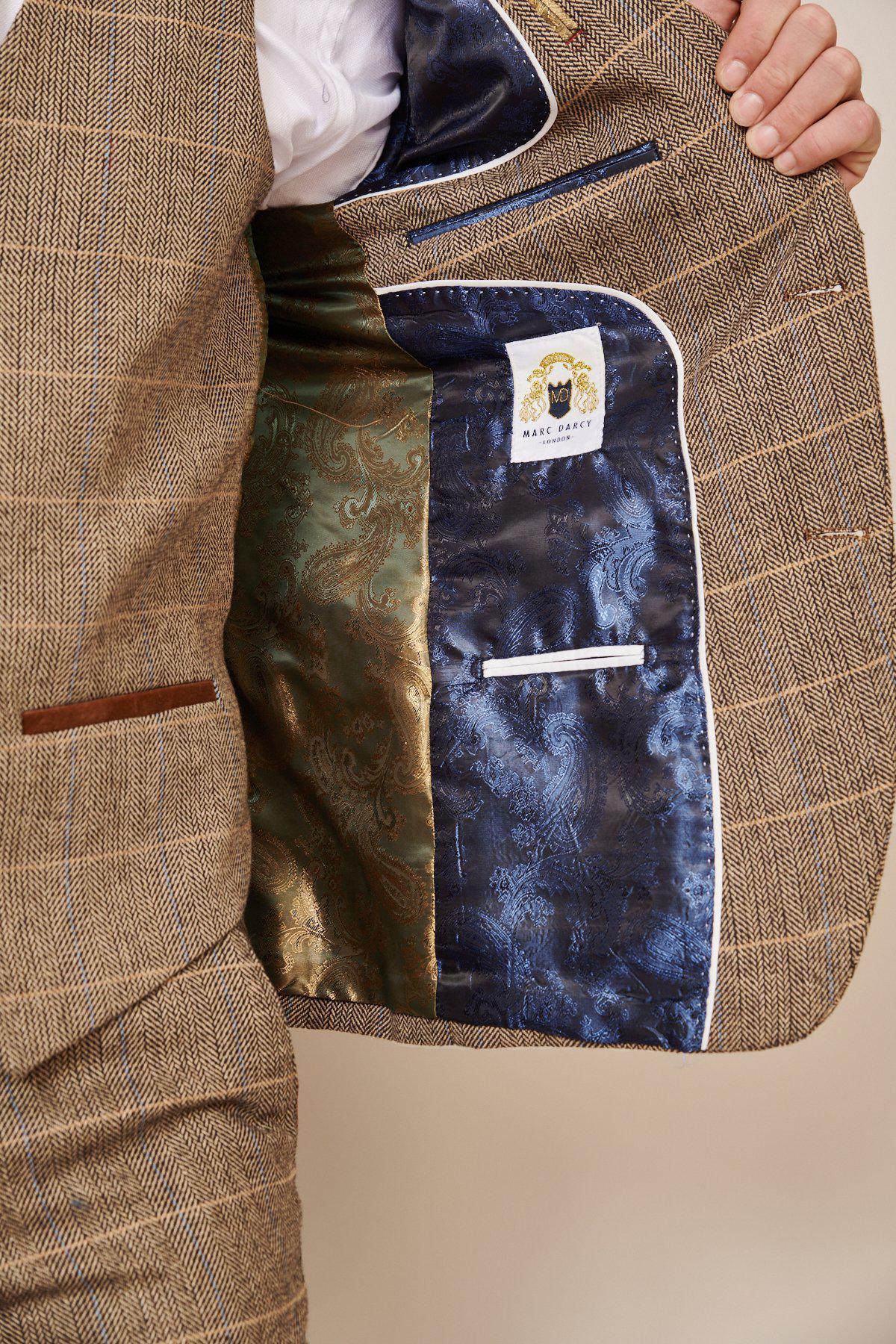 A person holds open the marcdarcy WHU Collection - TED Tan Tweed Suit With Dion Waistcoat, revealing a vibrant green and blue paisley lining and a white “MAKE JACKET” label with a black dog logo, as worn by Lukasz Fabianski.