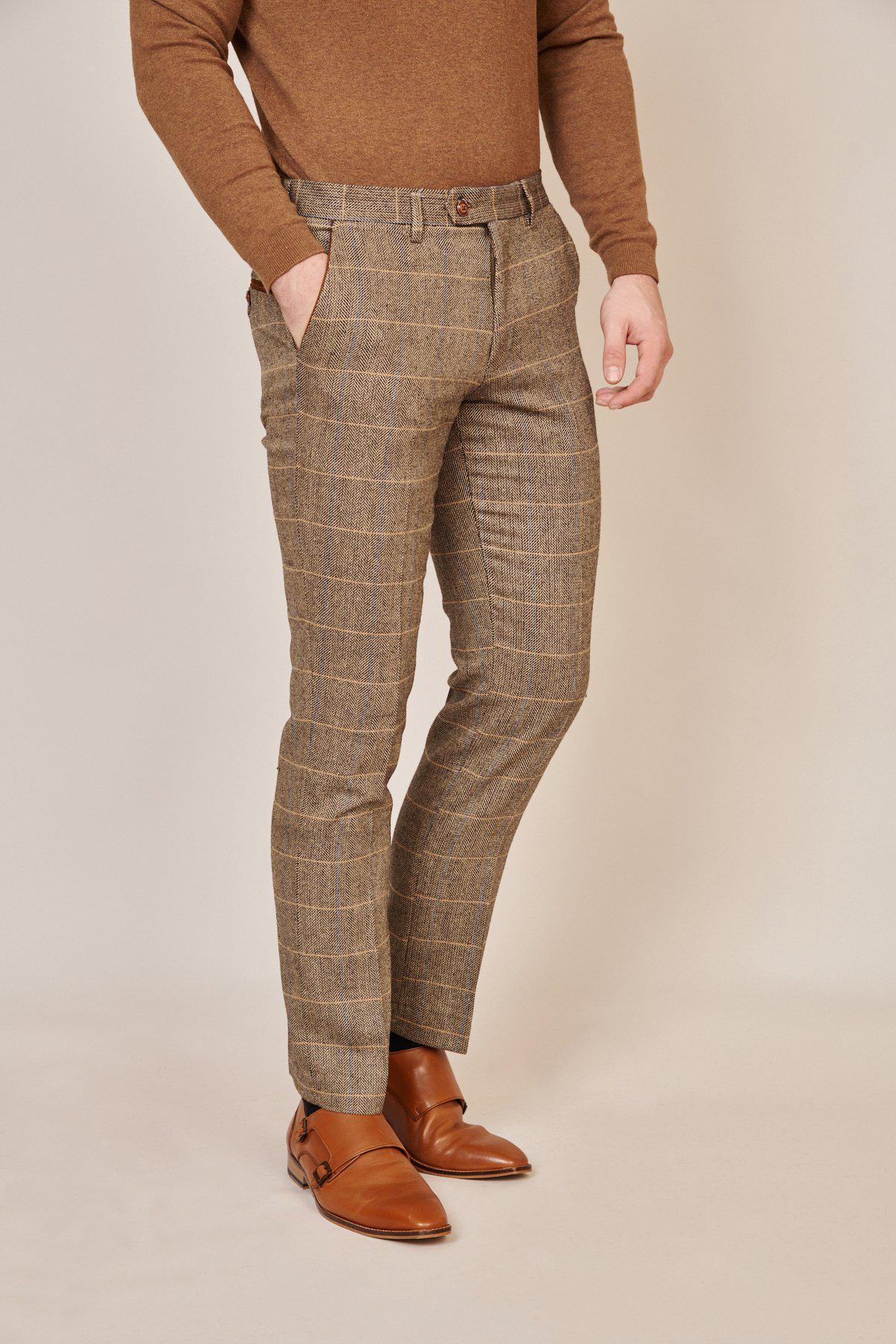 A person showcases English gent style in marcdarcy’s WHU Collection - TED Tan Tweed Check Three Piece Suit as worn by Lukasz Fabianski, posing with hands in pockets against a light background.
