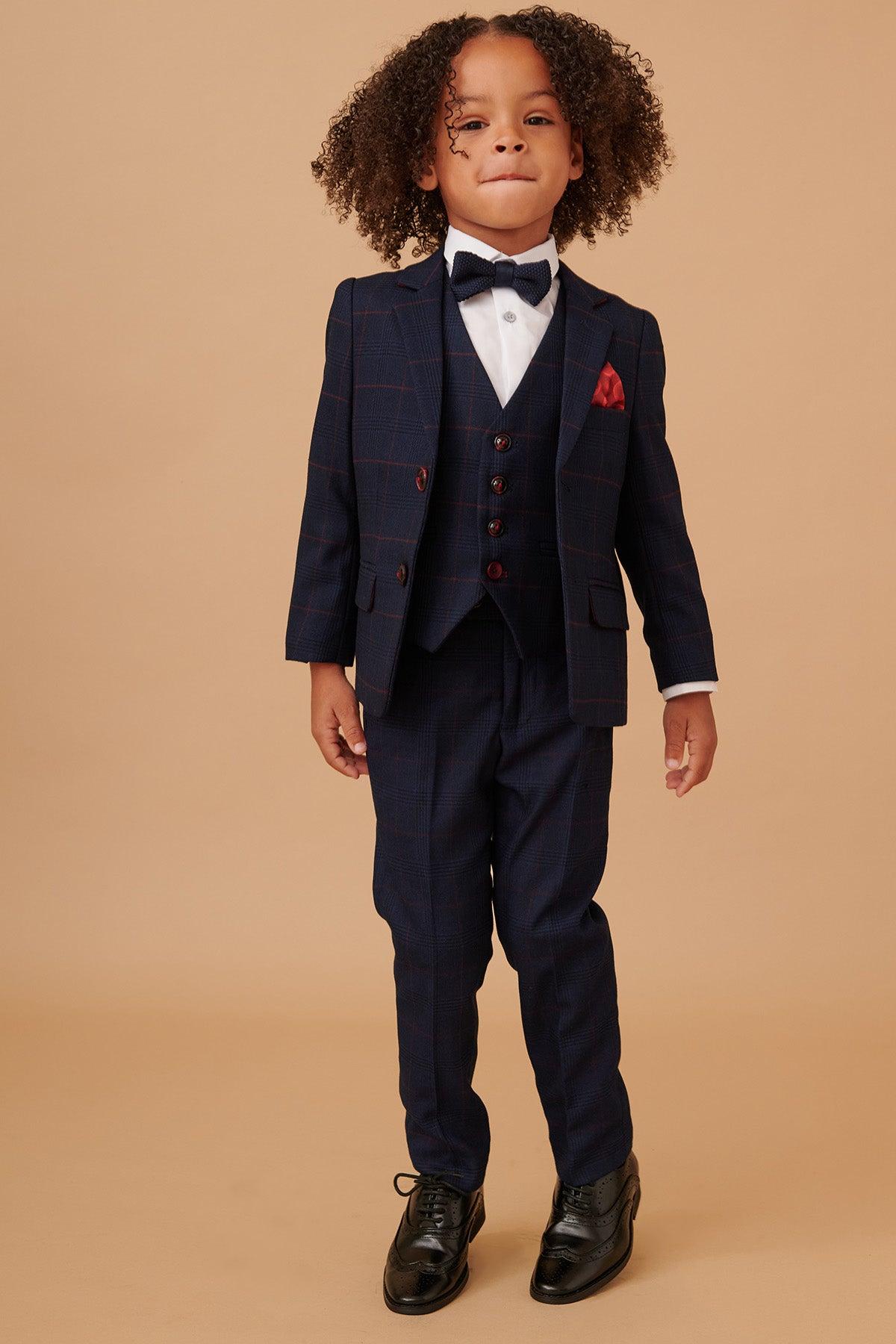 A young boy models the Marc Darcy EDINSON Children's Navy Wine Check Print Three Piece Suit, complete with a check blazer, red pocket square, bow tie, and dress shoes—ideal for special occasions.
