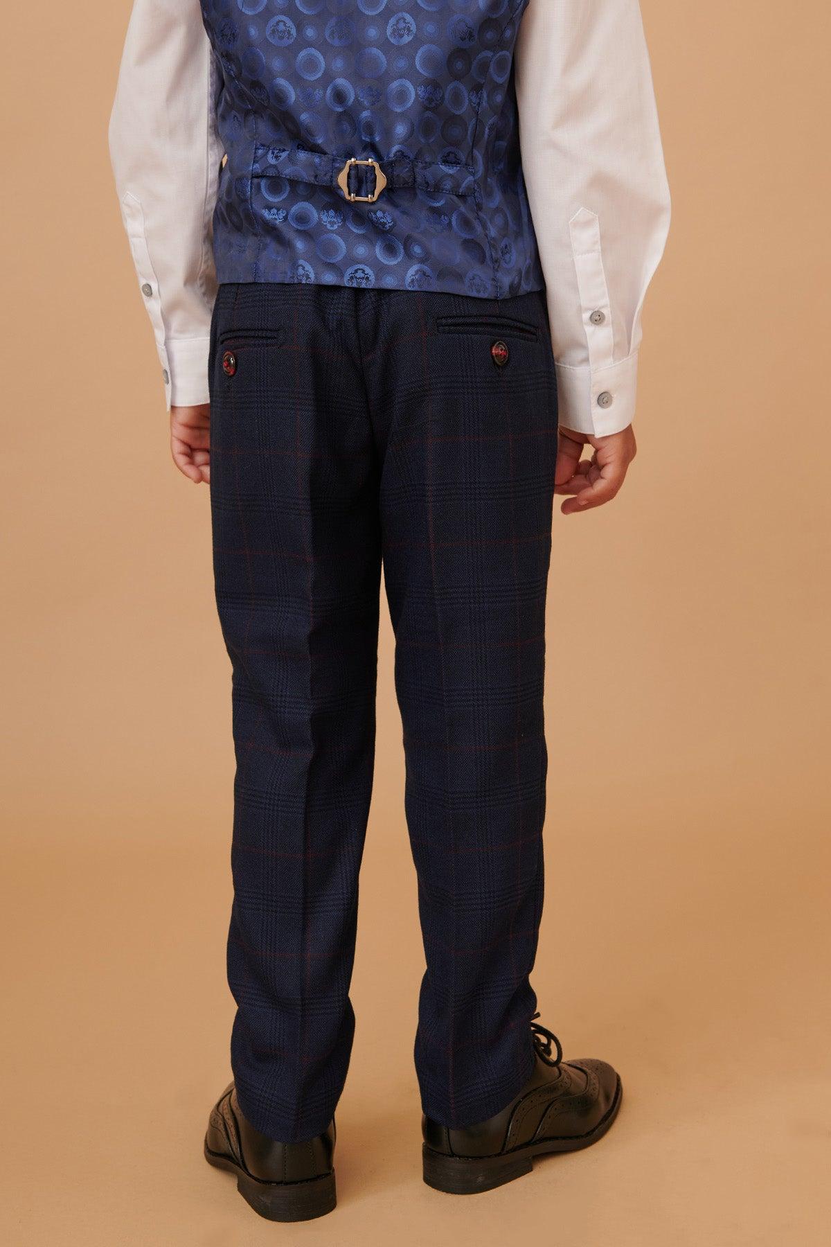 A child faces away, wearing the Marc Darcy EDINSON Childrens Navy Wine Check Print Three Piece Suit—white shirt, navy wine check vest with buckle, matching check trousers, and black dress shoes—set against a beige background.