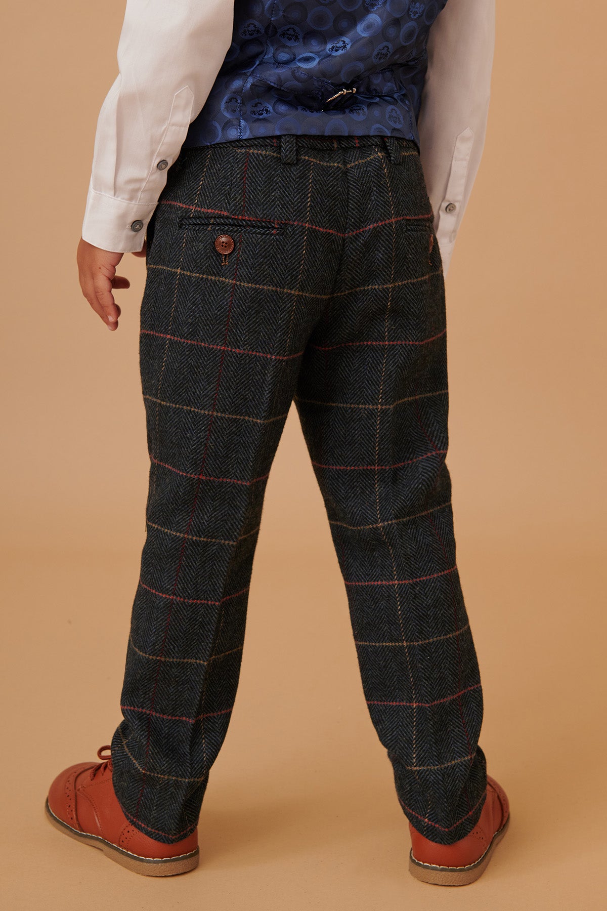 A child wearing the marcdarcy ETON Children's Navy Blue Tweed Check Three Piece Suit stands with their back to the camera against a beige background.