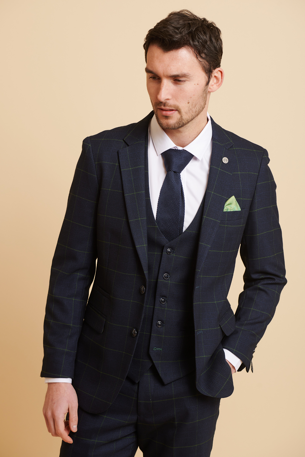 A man in the Marc Darcy EDINSON navy green check three piece suit, paired with a white shirt, navy tie, and green pocket square, stands against a cream background.
