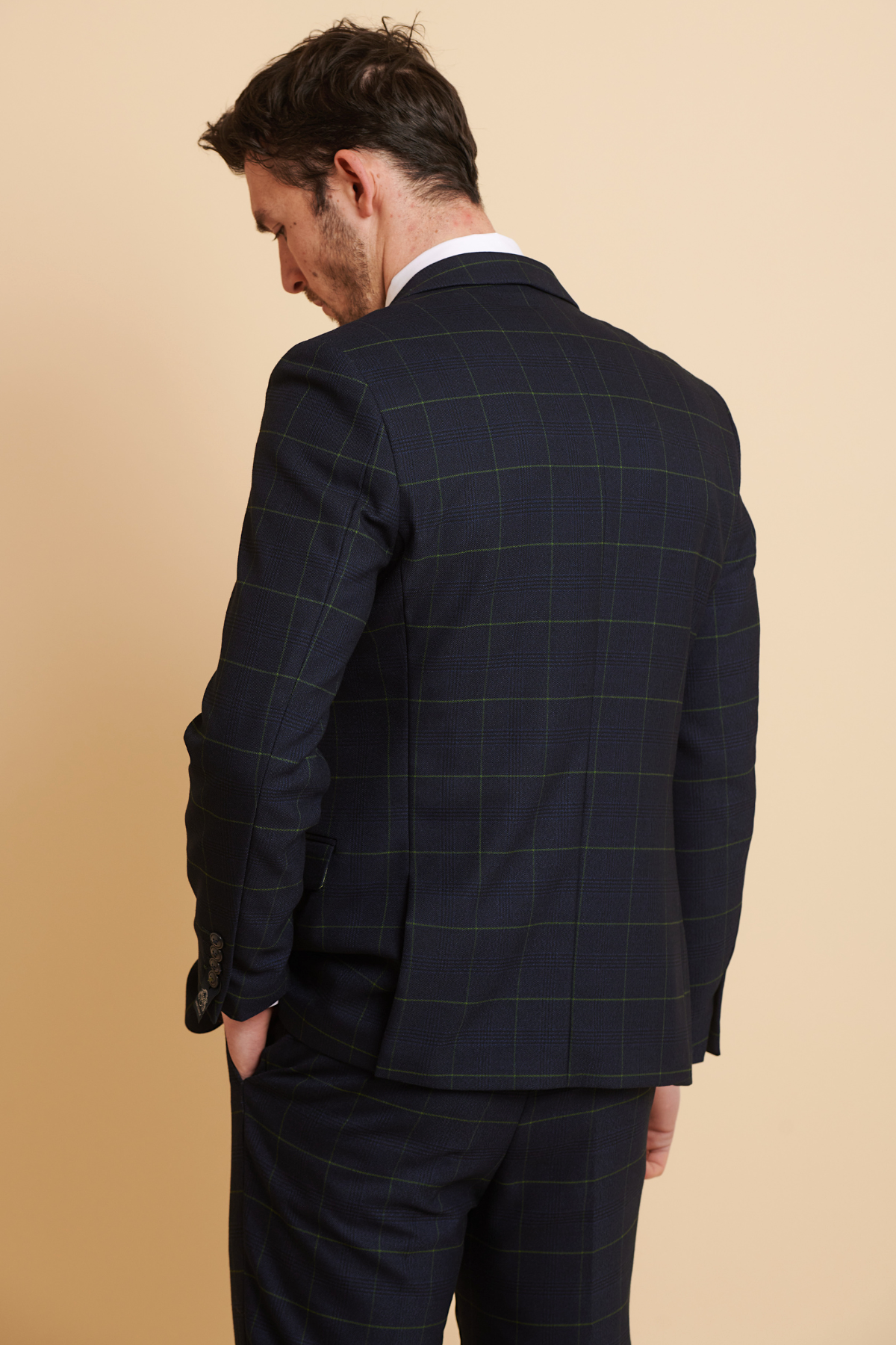 Back view of a man wearing the Marc Darcy EDINSON Navy Green Check Three Piece Suit in slim fit, featuring green Prince of Wales check, paired with a white shirt, set against a beige background.