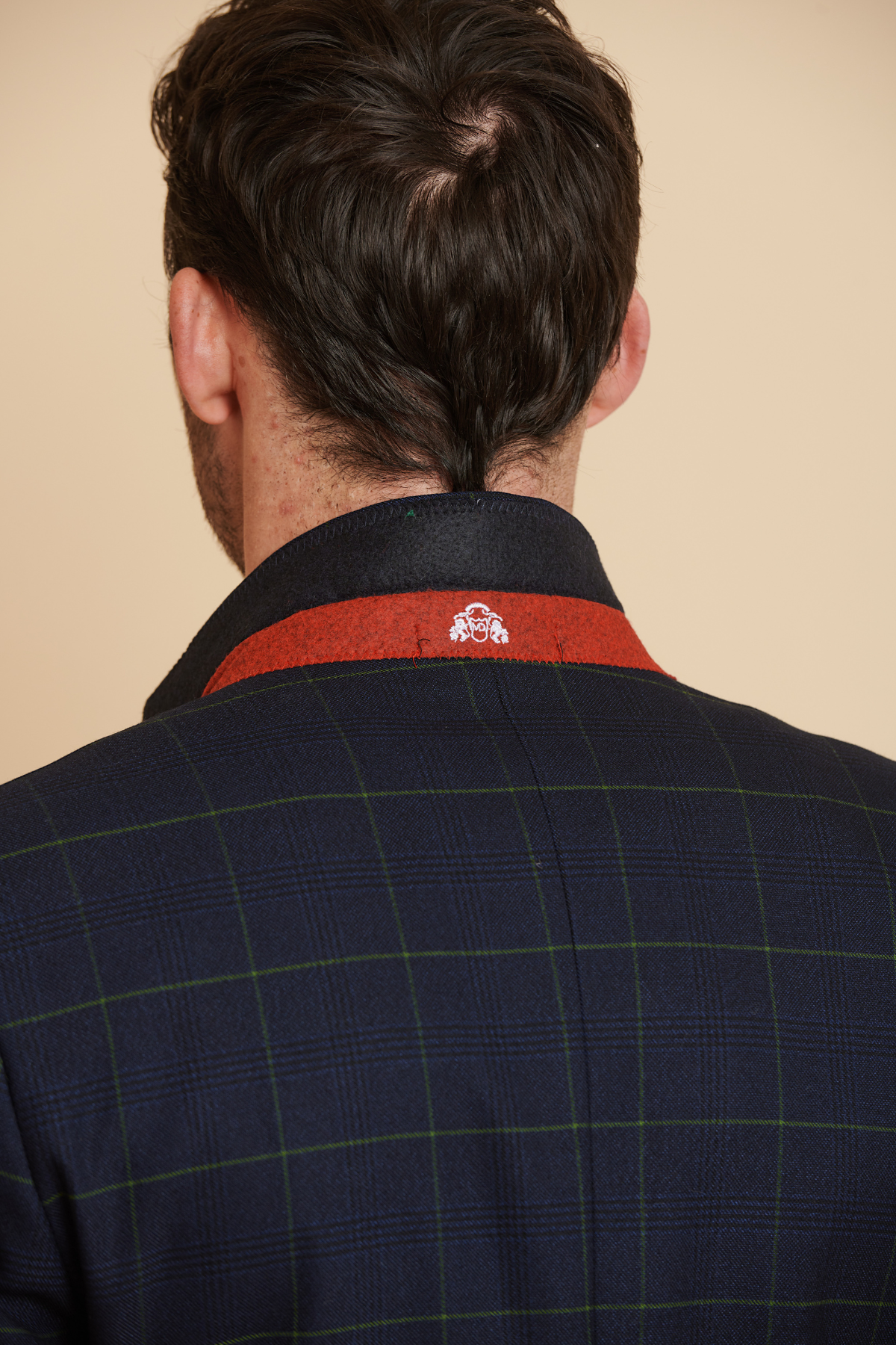 A man with dark hair is seen from behind wearing the Marc Darcy Everton Collection James Tarkowski in EDINSON navy green check suit, featuring a red collar detail and a white embroidered emblem on the back.