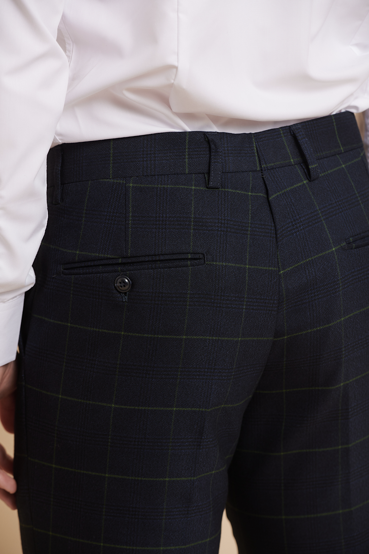 Close-up of a person wearing Marc Darcy's EDINSON navy green check trousers, featuring a white shirt and a black button on the back pocket.