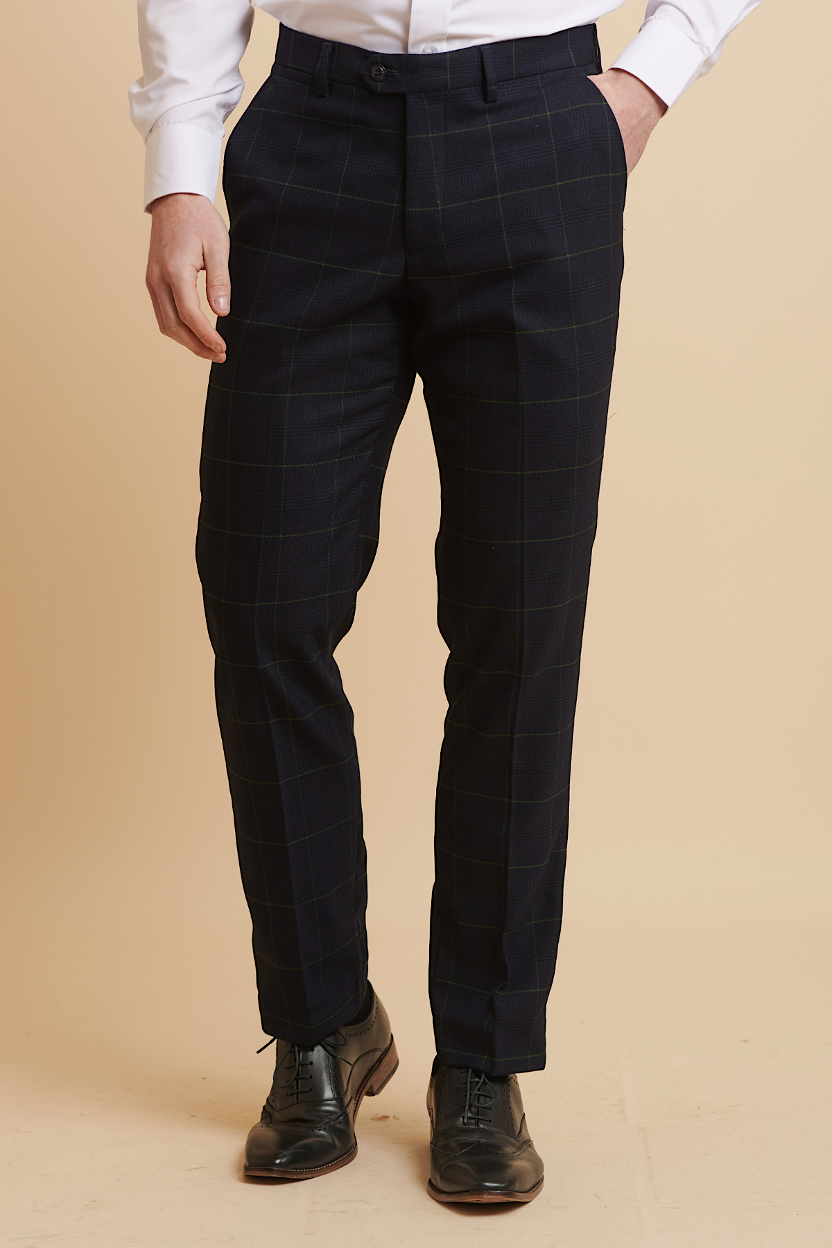 A man wears Marc Darcy’s EDINSON Navy Green Check Trousers, featuring a subtle green windowpane, paired with a white shirt and black oxford brogues against a beige background.