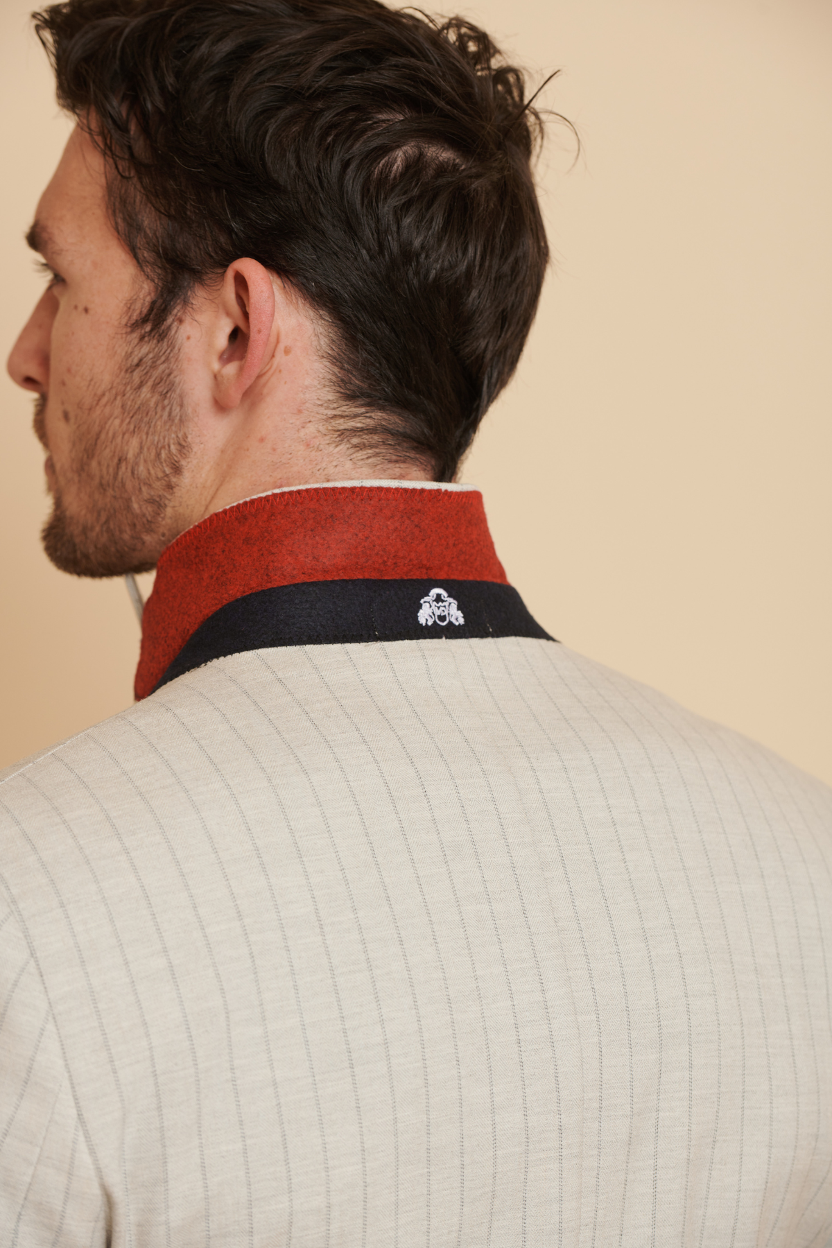 Close-up of a man wearing The Everton Collection | Beto In GRANT Stone Pinstripe Double Breasted Suit by Marc Darcy, featuring a cream pinstripe jacket with a red and black collar.
