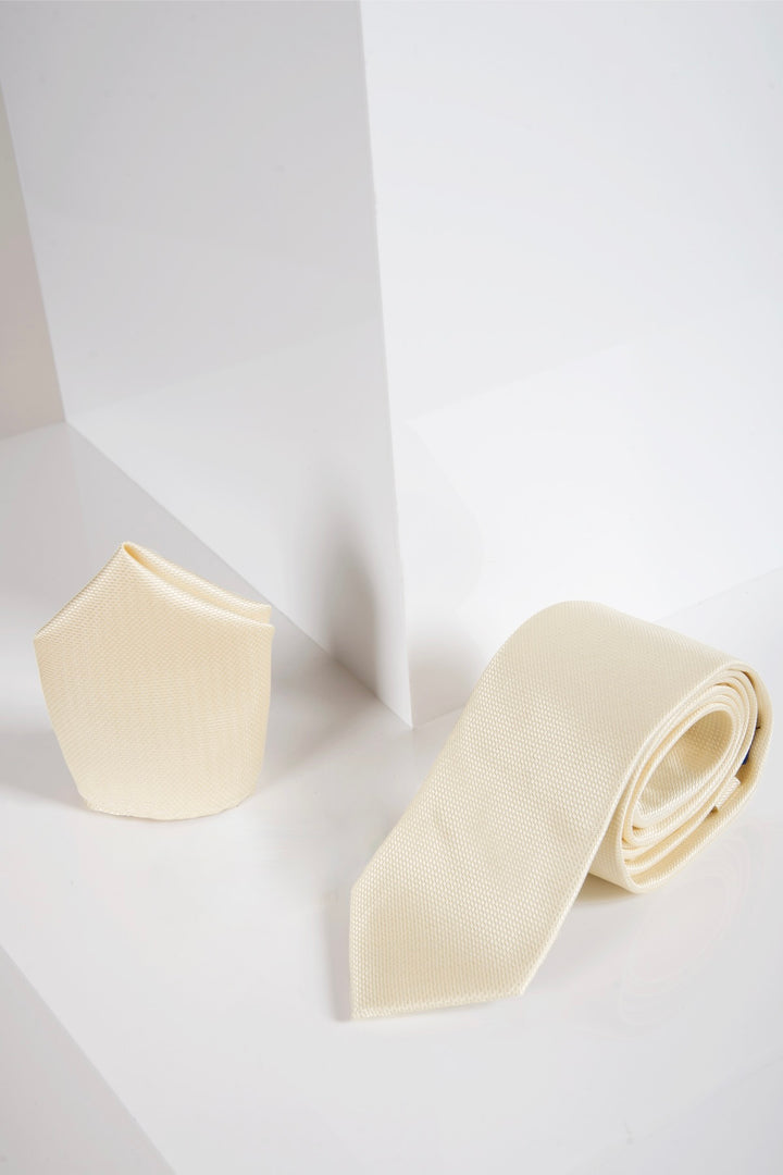 The Accessory TB17 Birdseye Tie and Pocket Square Set in Yellow, featuring a textured necktie and matching pocket square, is displayed upright on a glossy white surface with geometric white background panels.