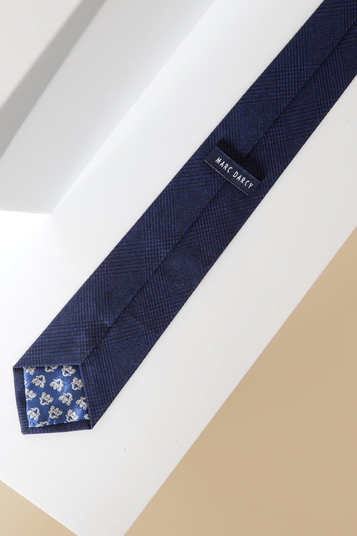 The BROMLEY - Navy Check Tie by Accessory features a textured navy blue fabric with a subtle Prince of Wales check and blue patterned lining at the tip.