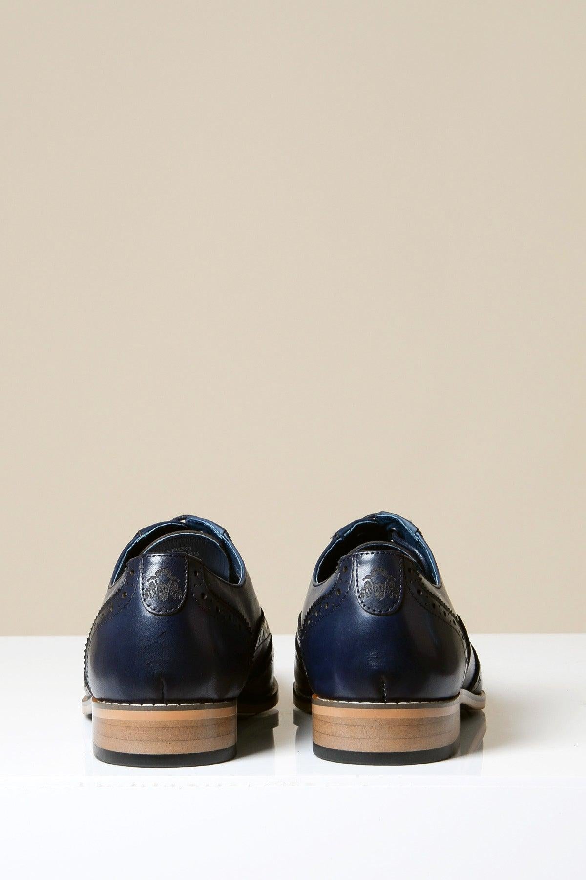 The MARCO Navy Blue Leather Oxford Wingtip Shoes by Marc Darcy, crafted from full grain leather with light brown soles, are shown from the back on a white surface against a beige background.