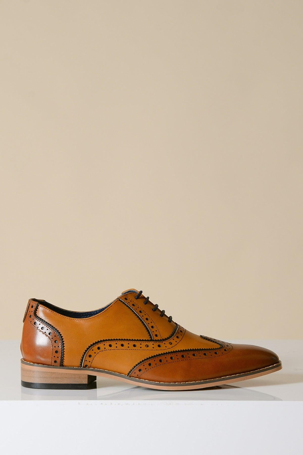 The MARCO - Tan Leather Oxford Wingtip Shoe by Marc Darcy features full grain leather with brogue perforations, hand-stitched details, black laces, and a low stacked heel, displayed on a white surface against a beige background.