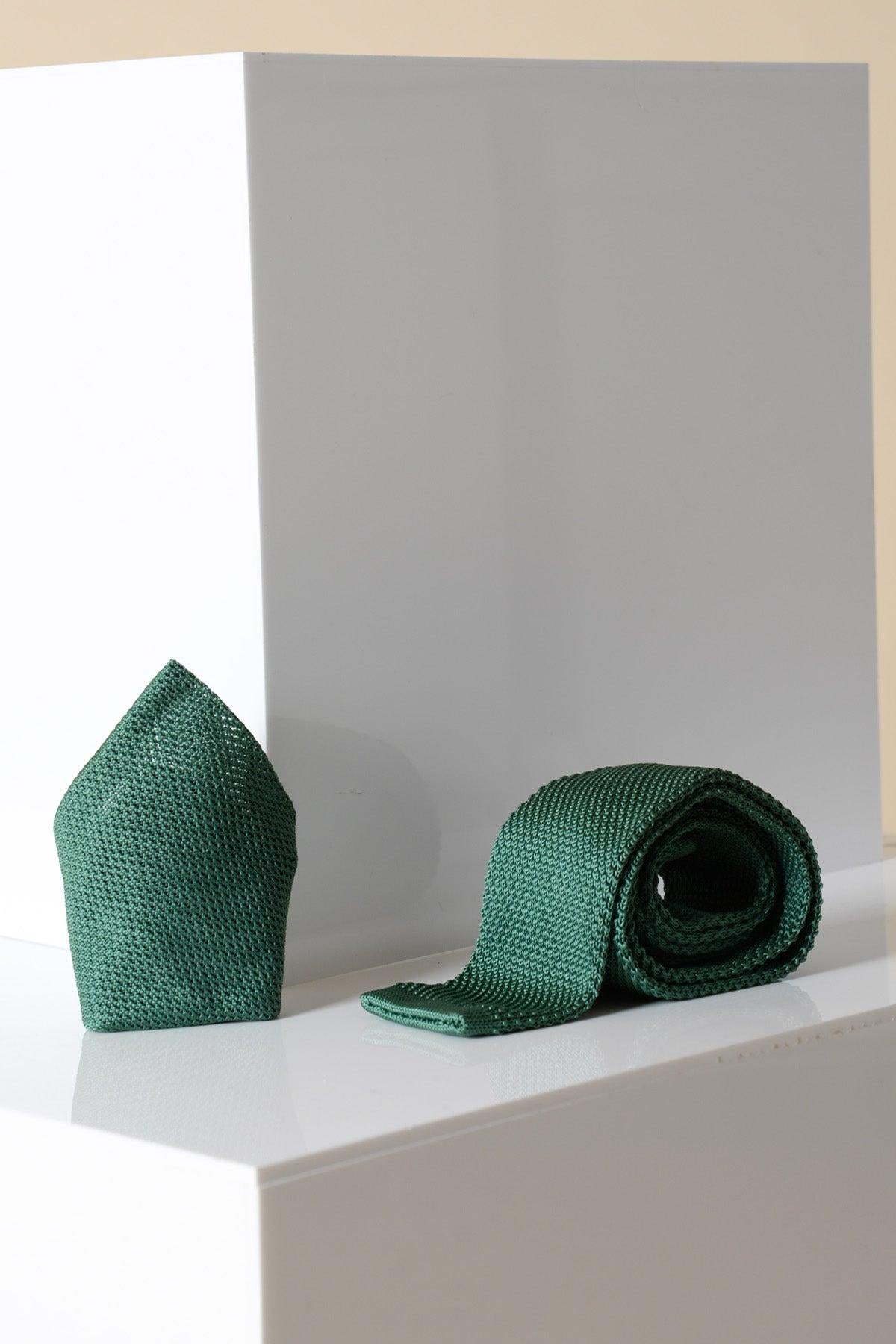 The KT - Olive Knitted Tie & Pocket Square by Accessory is displayed on white geometric surfaces, featuring a modern textured olive green tie and a folded pocket square against a neutral background.