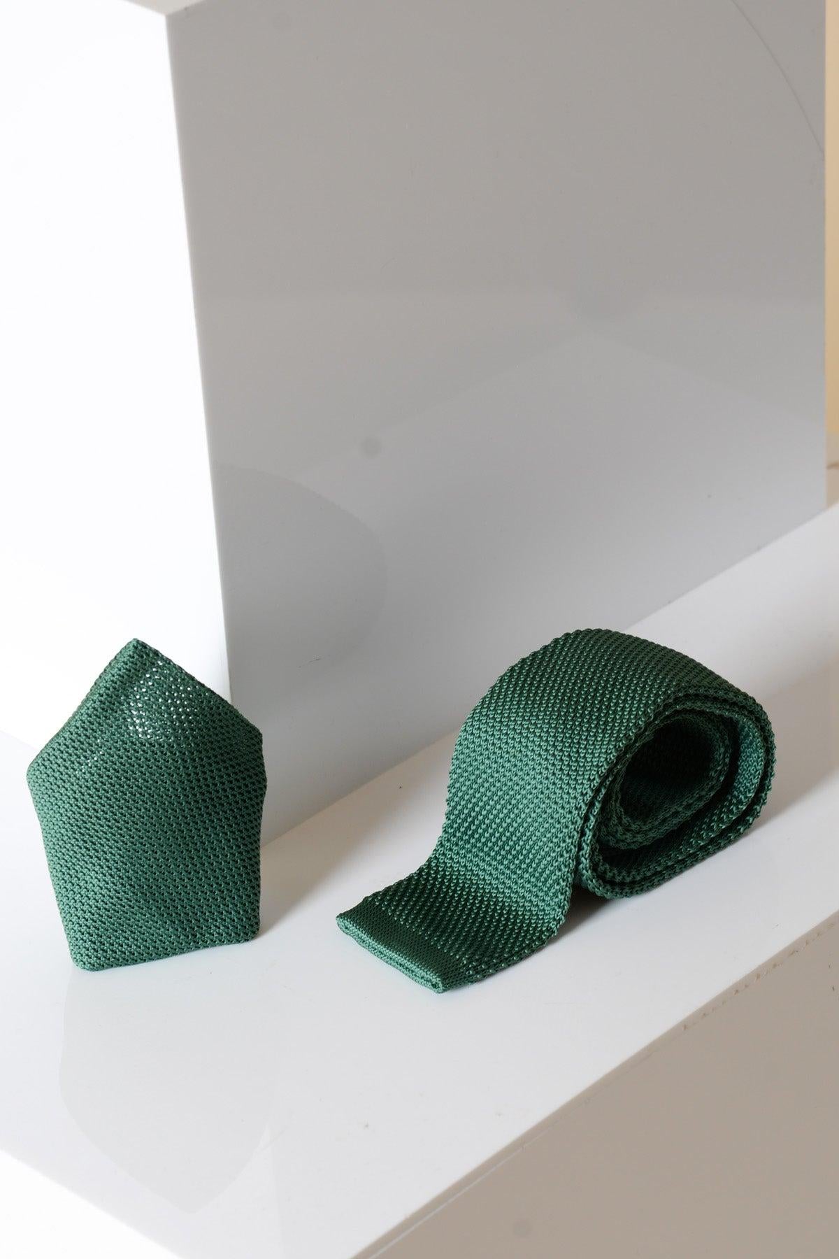 The Accessory KT - Olive Knitted Tie & Pocket Square displays a modern textured design, with both items in olive green arranged on a glossy white surface against geometric white accents.
