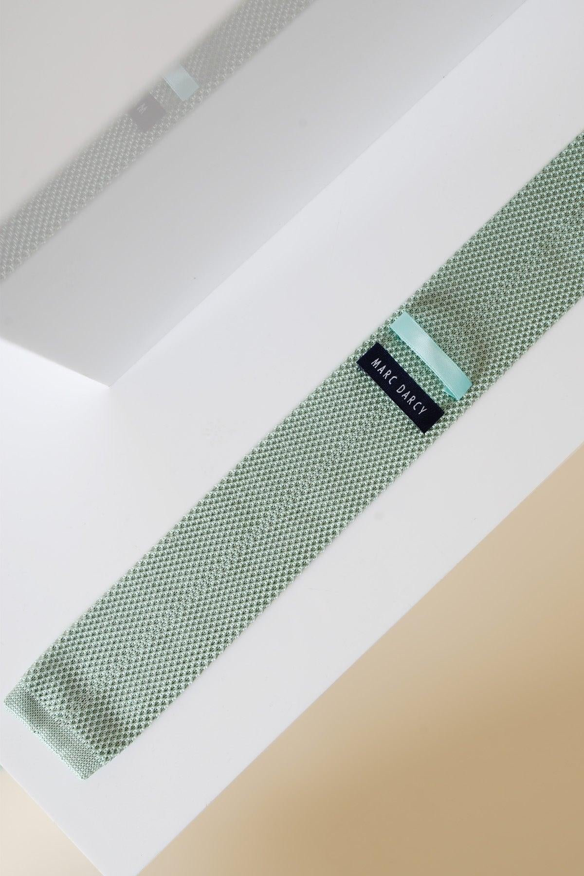 The Accessory KT - Green Knitted Tie & Pocket Square features a sage green textured knit tie, laid flat on a white surface with its reflection visible. The MAKE ORACLE label is prominently displayed.