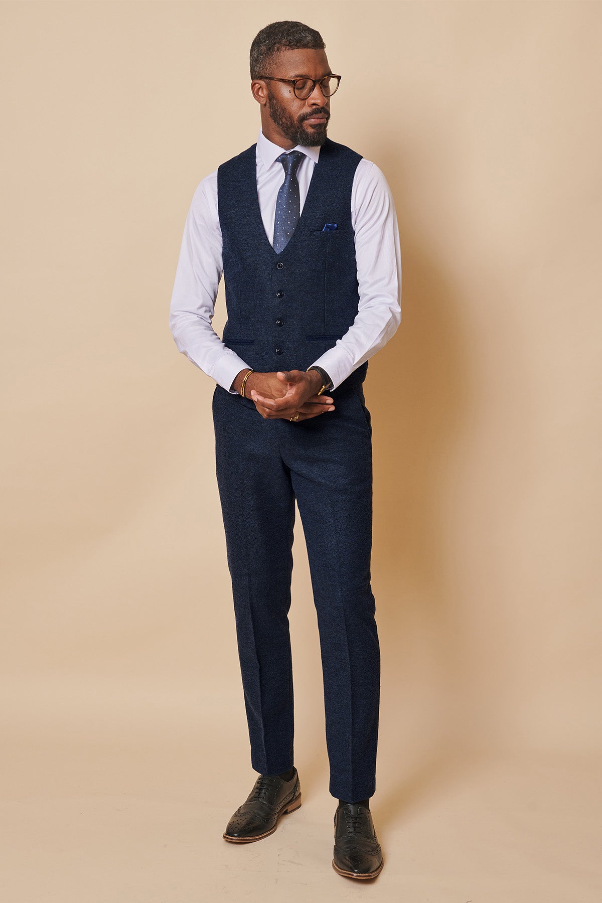 A Black man wearing glasses and a slim fit three-piece suit in the MARLOW Navy Tweed Single Breasted Waistcoat by marcdarcy, paired with a white shirt and polka-dot tie.