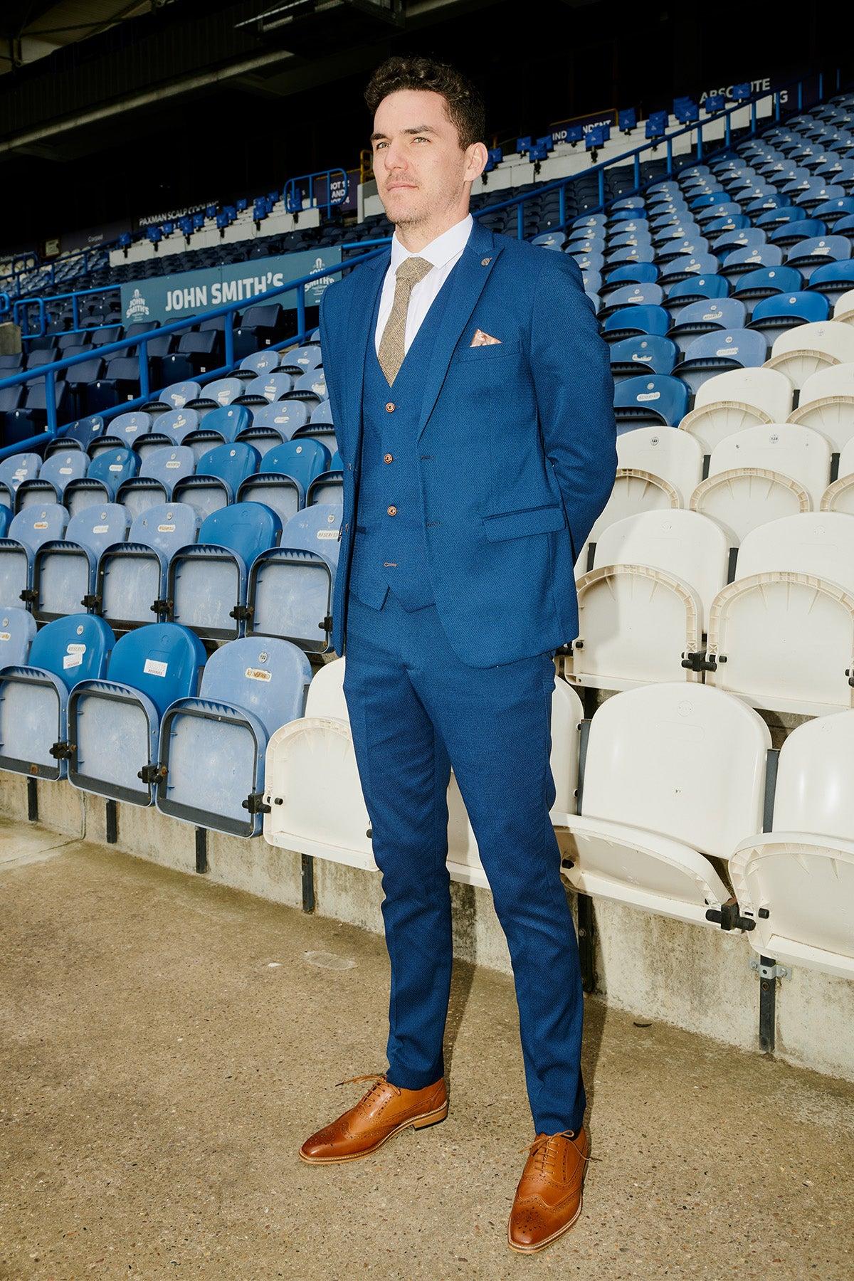 A man in a slim fit blazer and tan shoes stands in a stadium, echoing the style of the marcdarcy Huddersfield Town AFC | MAX Royal Blue Suit as worn by Lee Nicholls.