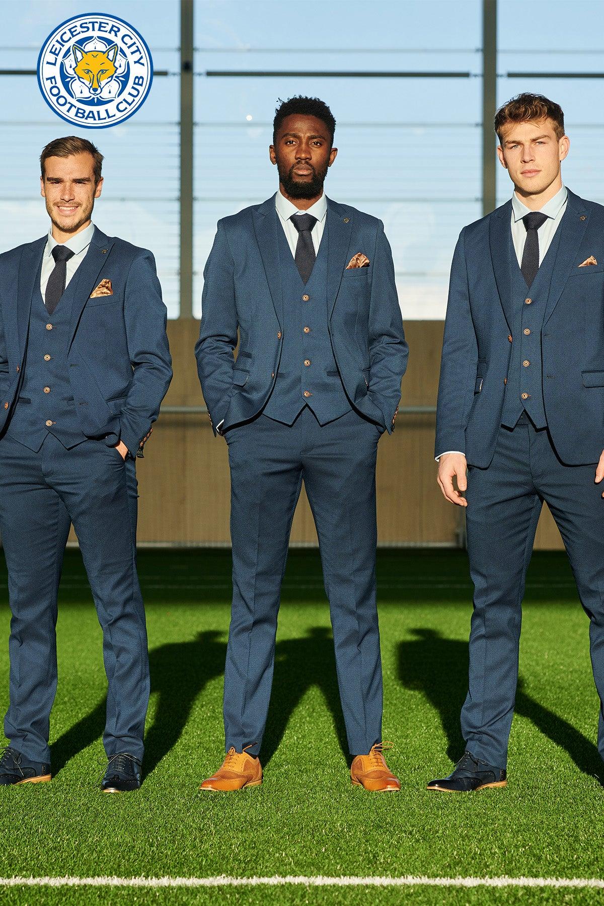 Three men wear marcdarcy Official Leicester City F.C. Club Suits (MAX Royal Blue) on a green field, with the club’s logo visible behind them.