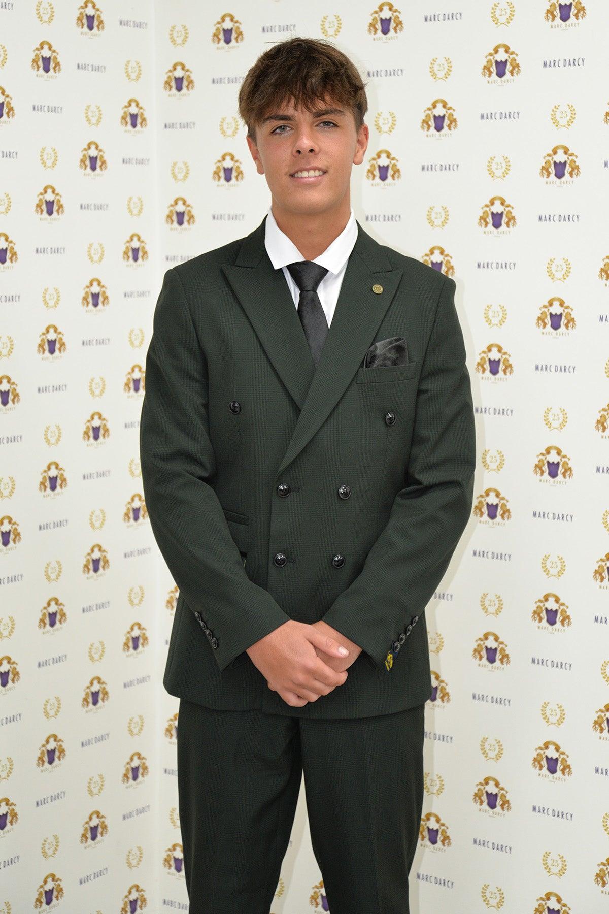 Coronation Street's Mason Radcliffe (Luca Toolan) poses and smiles in front of a Marc Darcy backdrop, wearing the BROMLEY Olive Green Double Breasted Two Piece Suit by Marc Darcy.