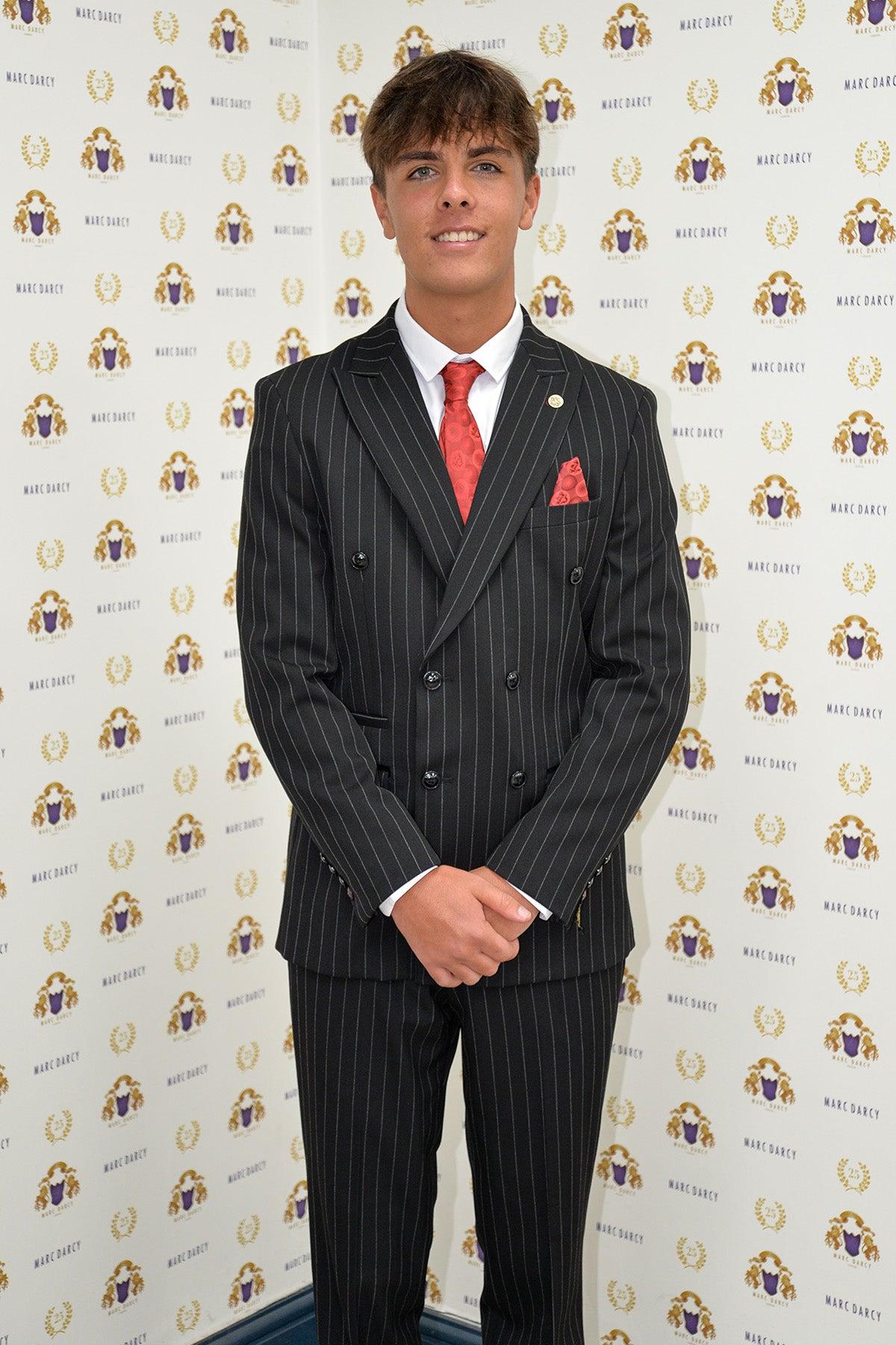 Luca Toolan (as Mason Radcliffe from Coronation Street) stands smiling in front of a step-and-repeat backdrop, wearing the Marc Darcy ROCCO Black Pinstripe Double Breasted Two Piece Suit with a white shirt and red patterned pocket square.