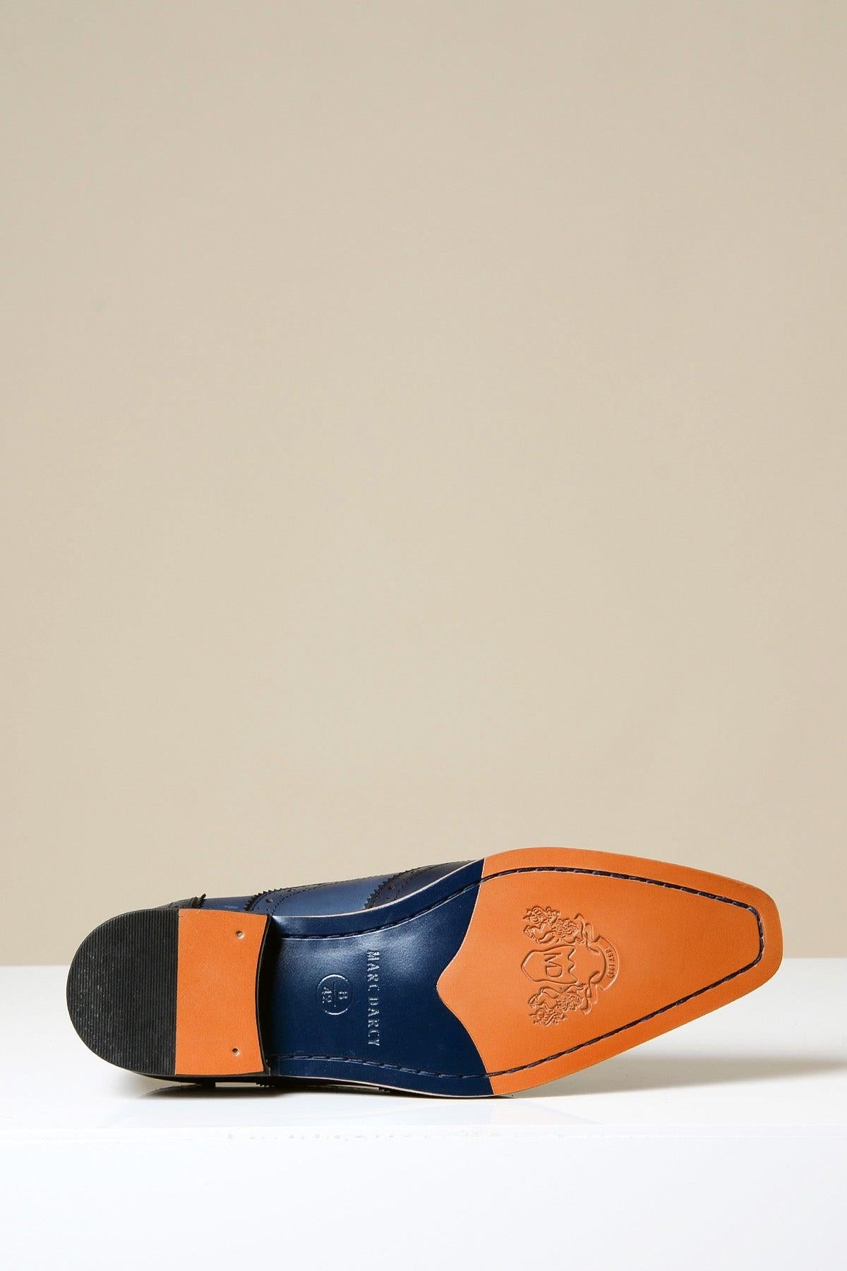 The MARCO Navy Blue Leather Oxford Wingtip Shoe by Marc Darcy is shown on its side, highlighting the tan hand-stitched sole with a rubber heel and embossed crest near the toe against a plain, light background.