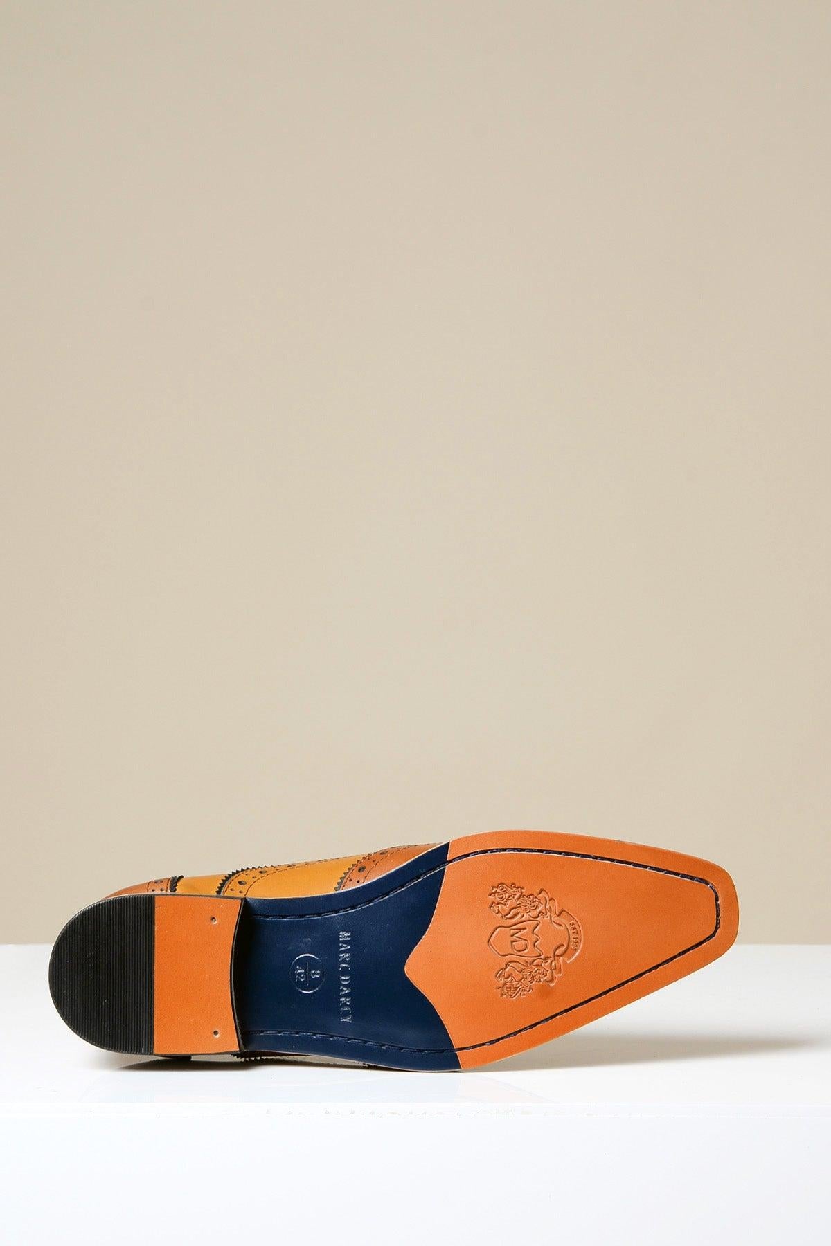 The MARCO Tan Leather Oxford Wingtip Shoe by Marc Darcy is shown on its side, revealing the hand-stitched tan full grain leather sole with a blue section and embossed design. The shoe rests on a white surface against a neutral background.