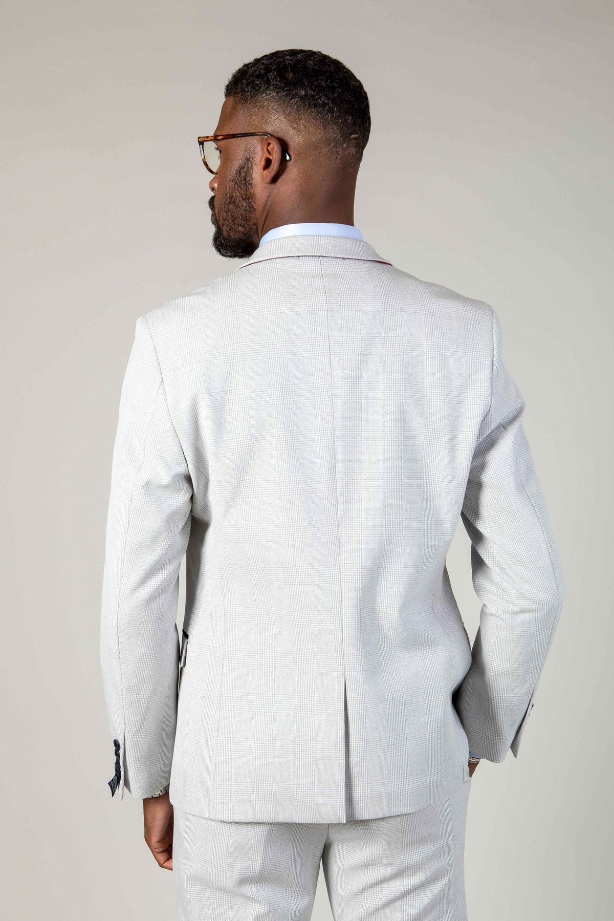 A man in the Marc Darcy WBA Collection - BROMLEY Stone Suit faces away from the camera, highlighting the back of his light gray jacket. He wears glasses and stands against a plain, light-colored background.