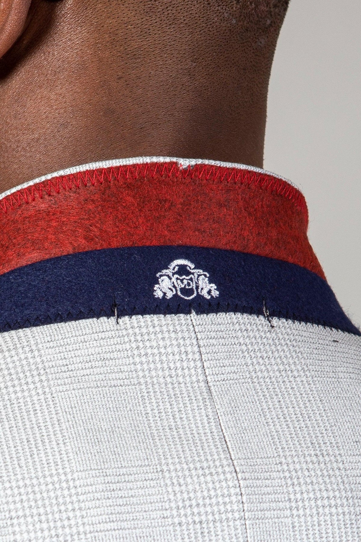 Close-up of the back collar of the Marc Darcy WBA Collection - BROMLEY Stone Suit With Kelvin Navy Waistcoat, showcasing a red and navy band, white embroidered logo, and Prince of Wales check on textured light gray fabric.