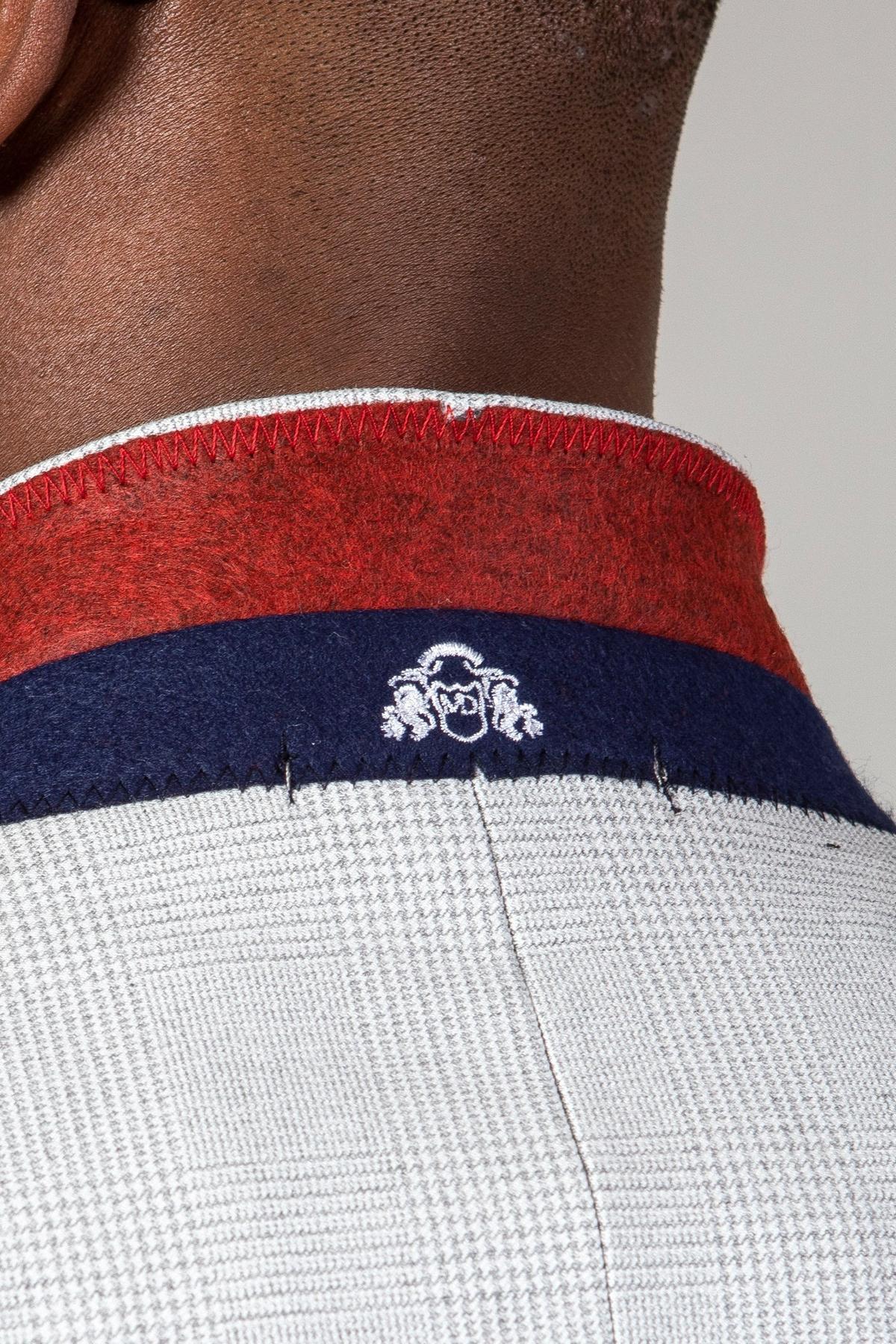 Close-up of the back of a person's neck wearing Marc Darcy's The WBA Collection - BROMLEY Stone Suit, featuring a white and gray Prince of Wales check pattern, red and navy collar, and a small white embroidered emblem below the collar.