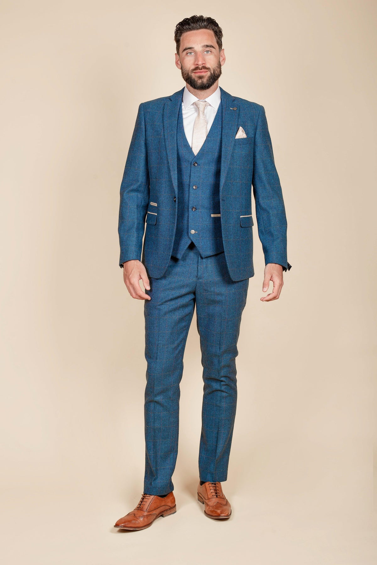 Ashley Young models The Everton Collection by marcdarcy in a DION Blue Tweed Check Suit with a white shirt, light tie, and brown dress shoes, standing against a beige background.