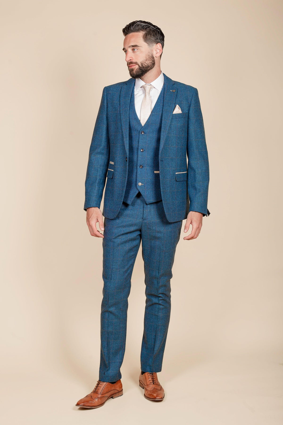 A man with a beard, looking to the side, wears the marcdarcy WHU Collection - DION Blue Tweed Check Suit as worn by Crysencio Summerville, paired with a light shirt and tie.