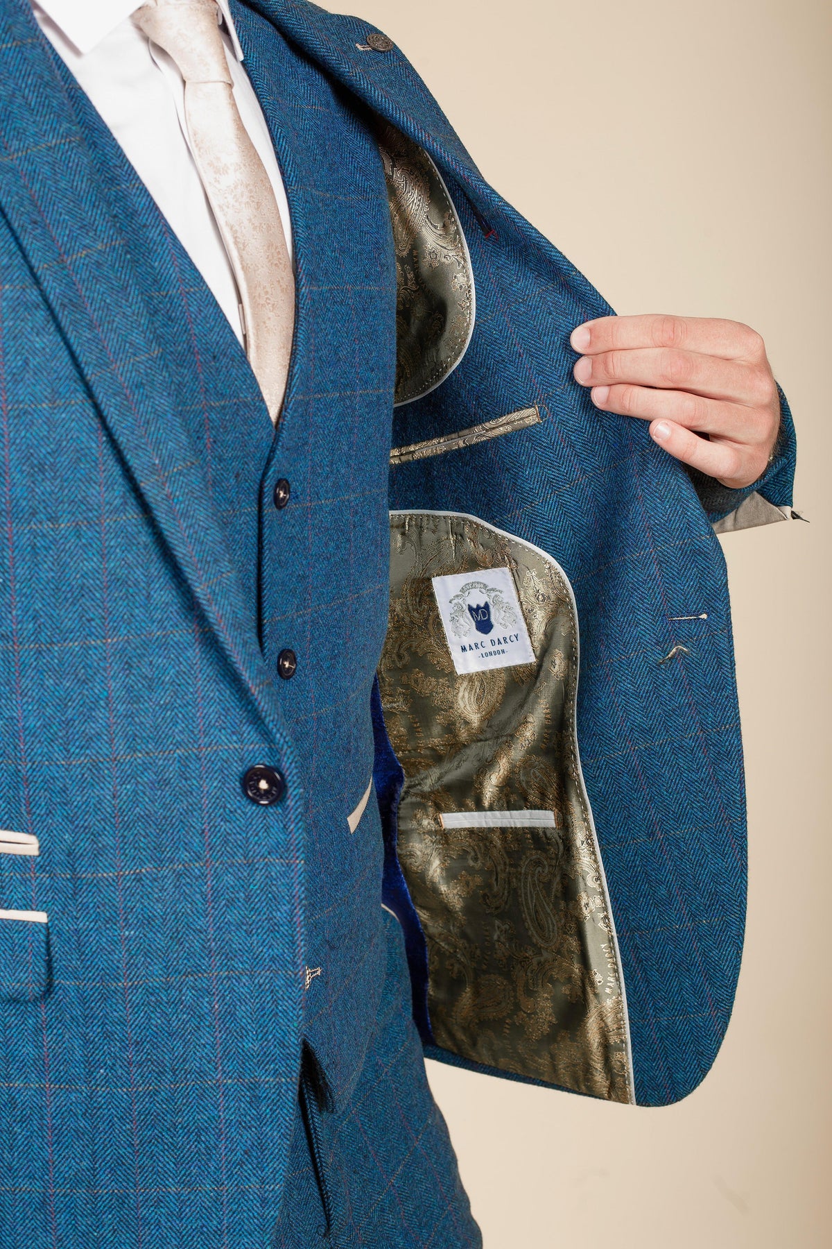 A man wears the marcdarcy Everton Collection Jarrad Branthwaite in DION Blue Tweed Check Suit, featuring a champagne paisley lining and matching tie, while a hand adjusts the lapel.